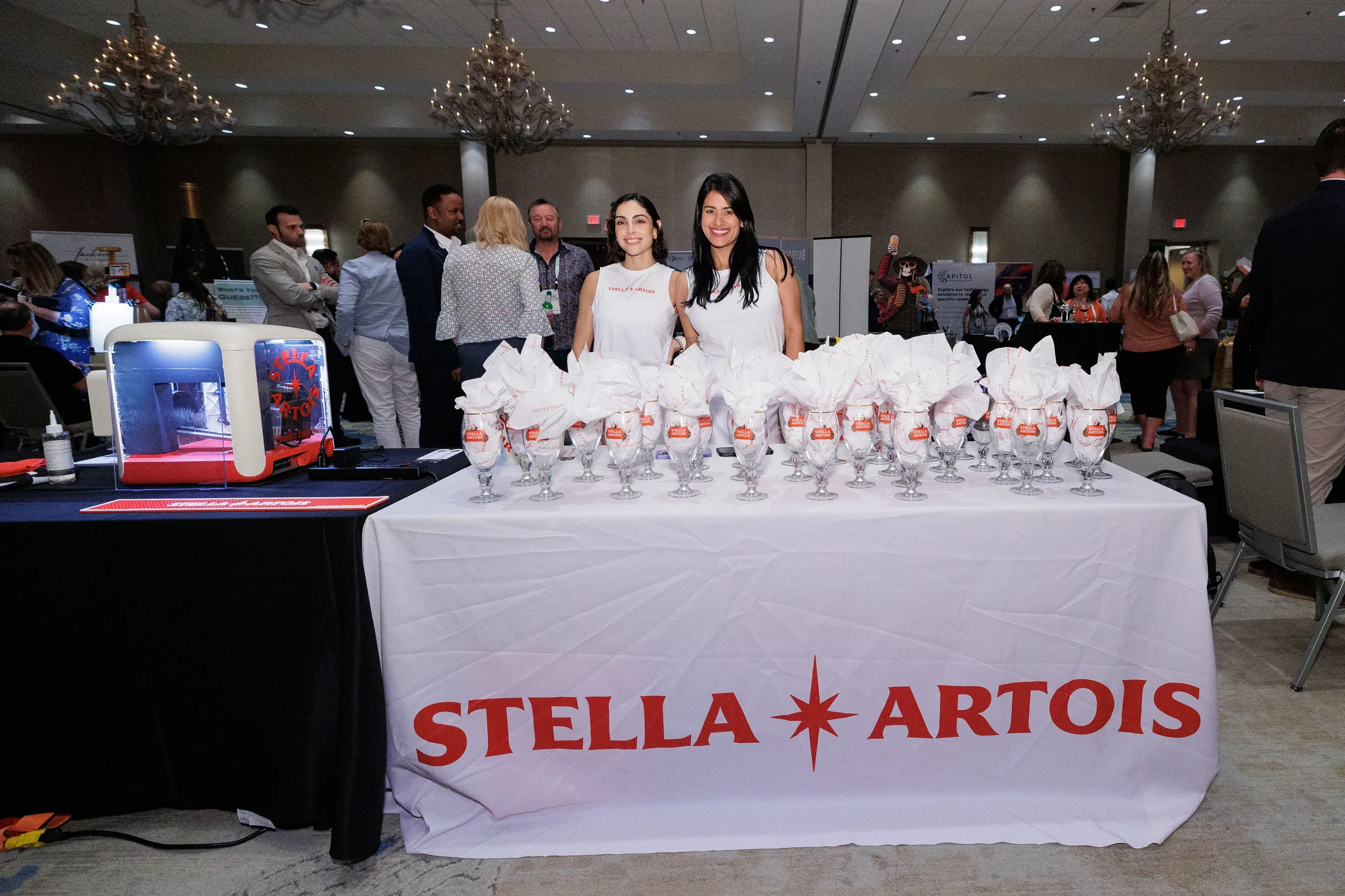 Two booth staff smile behind rows of branded glassware at Chicago industry conference expo floor