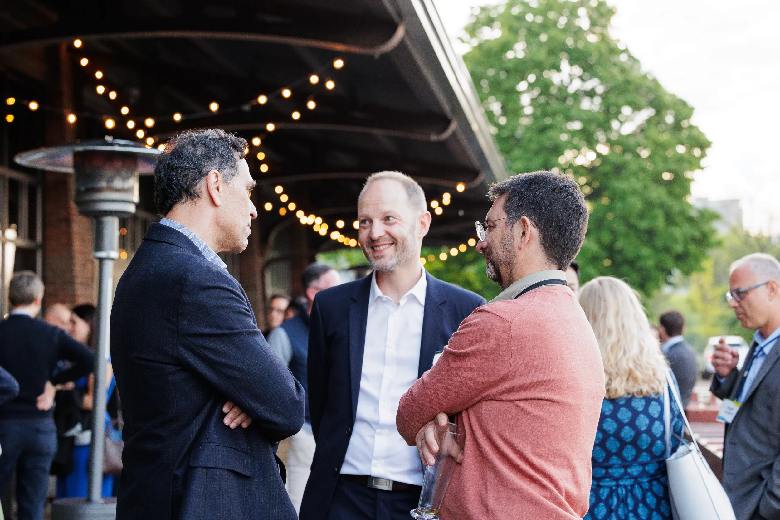 Three attendees network under string lights on outdoor patio at Orlando evening reception