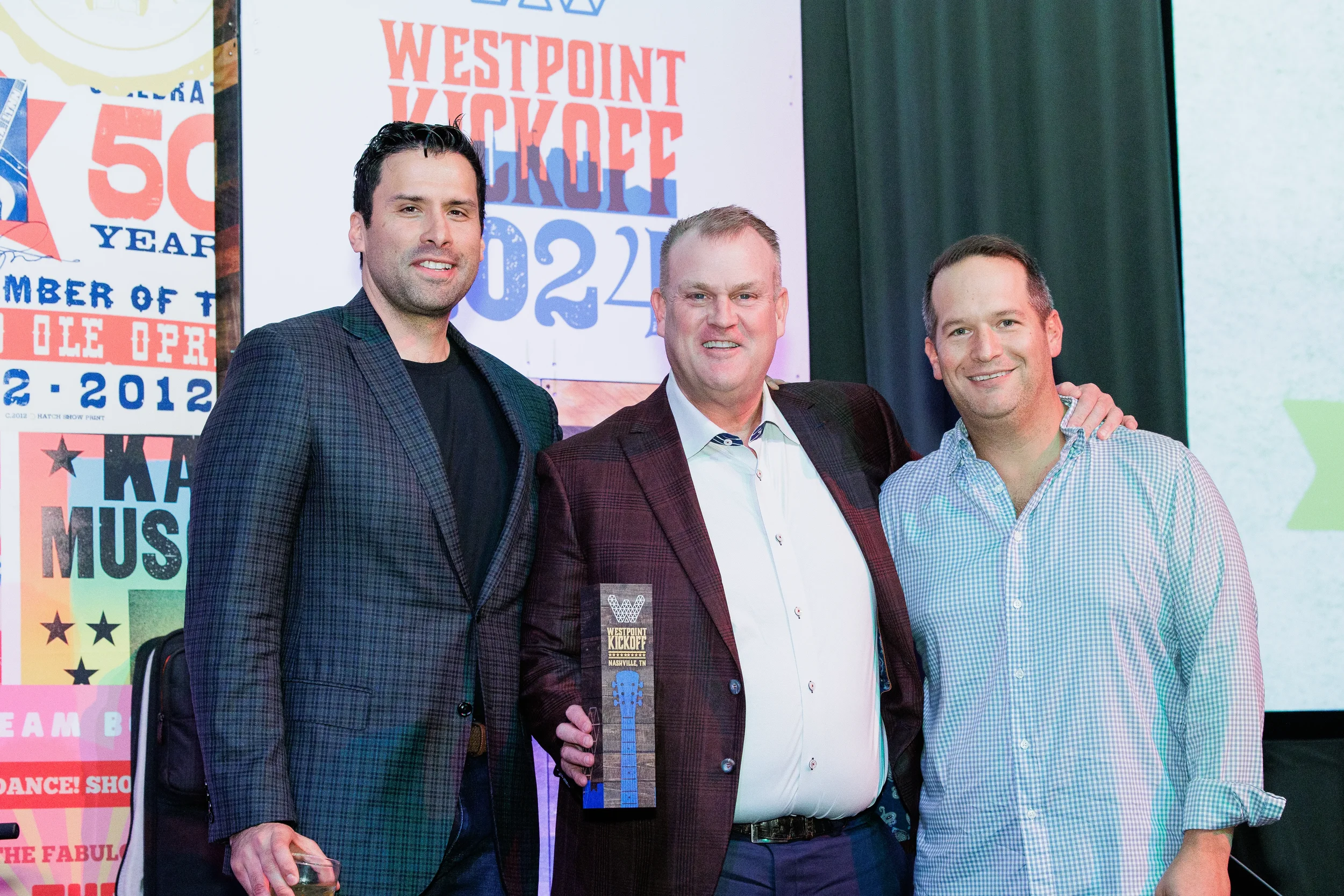 Three men pose on stage with award trophy in front of branded backdrop at Chicago corporate conference
