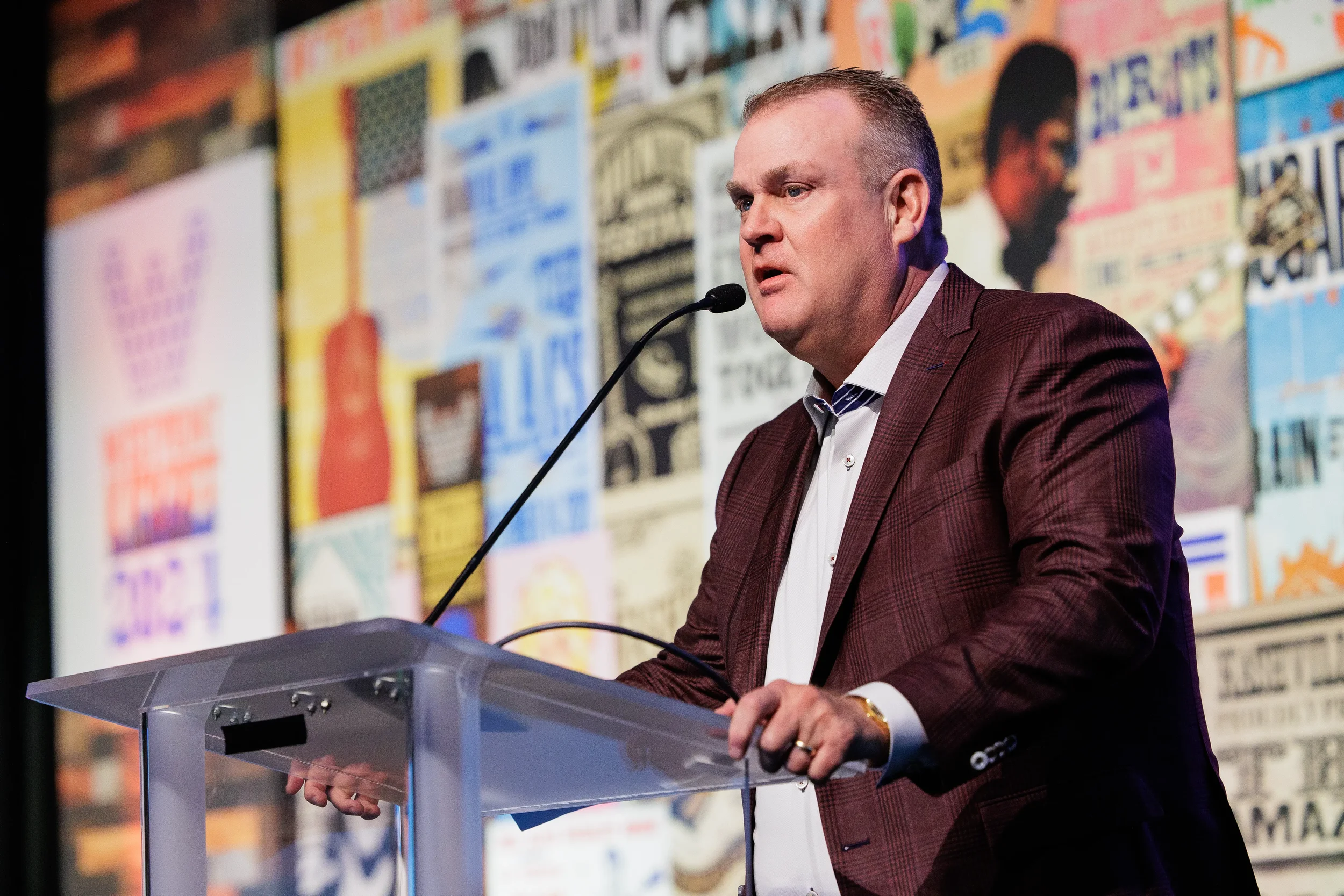 Speaker addresses audience from acrylic podium in front of colorful stage backdrop at Chicago corporate conference