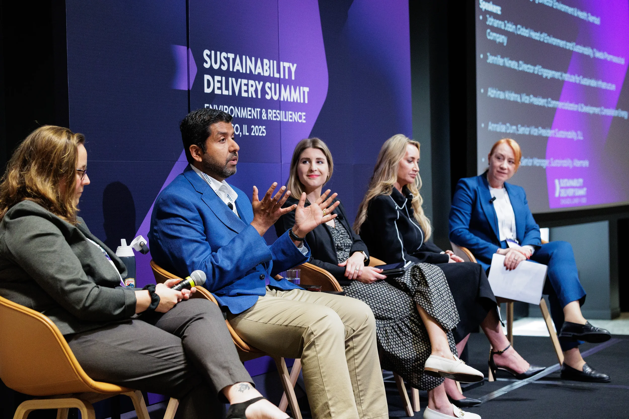 Panelist gestures while speaking among five panelists on branded stage at Orlando summit