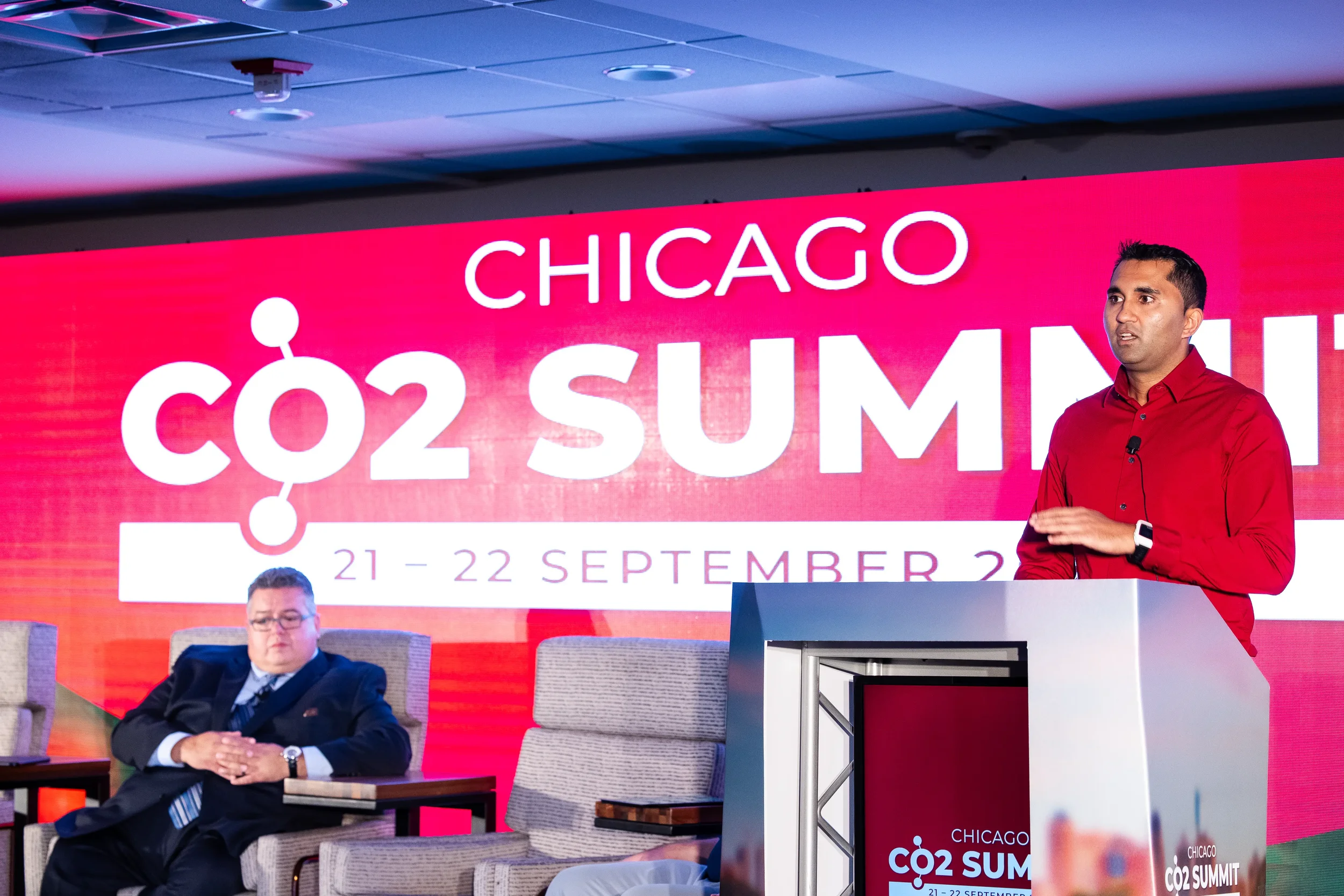 Speaker presents from podium on stage in front of branded backdrop at Orlando industry summit