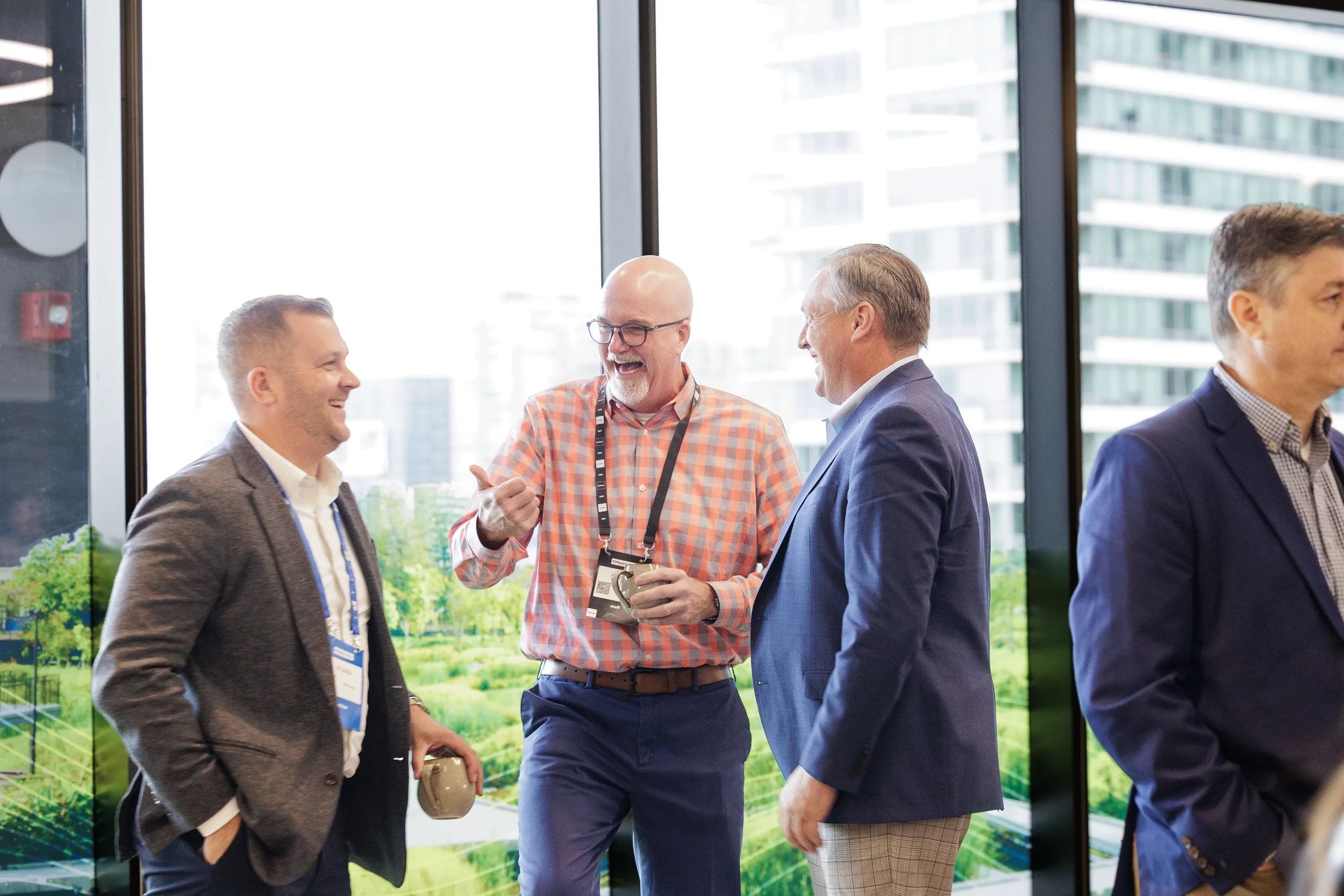 Attendees laugh together holding coffee mugs by windows during networking break at Chicago corporate event