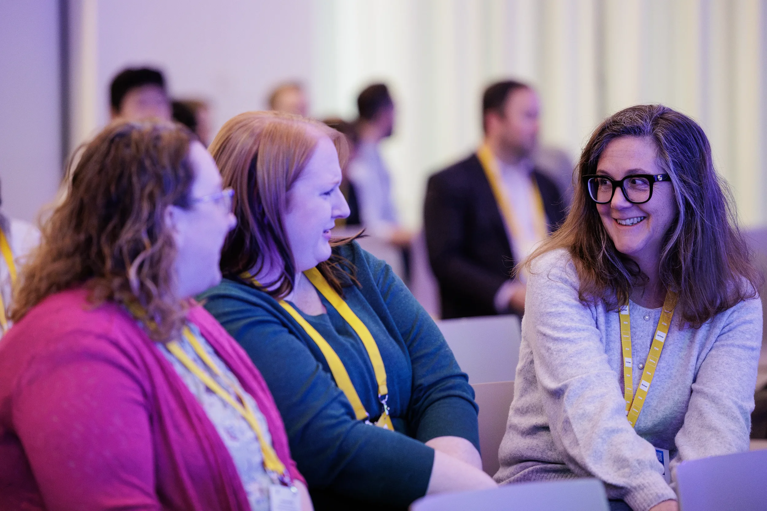 Smiling attendees chat while seated in purple-lit session room at Orlando corporate conference