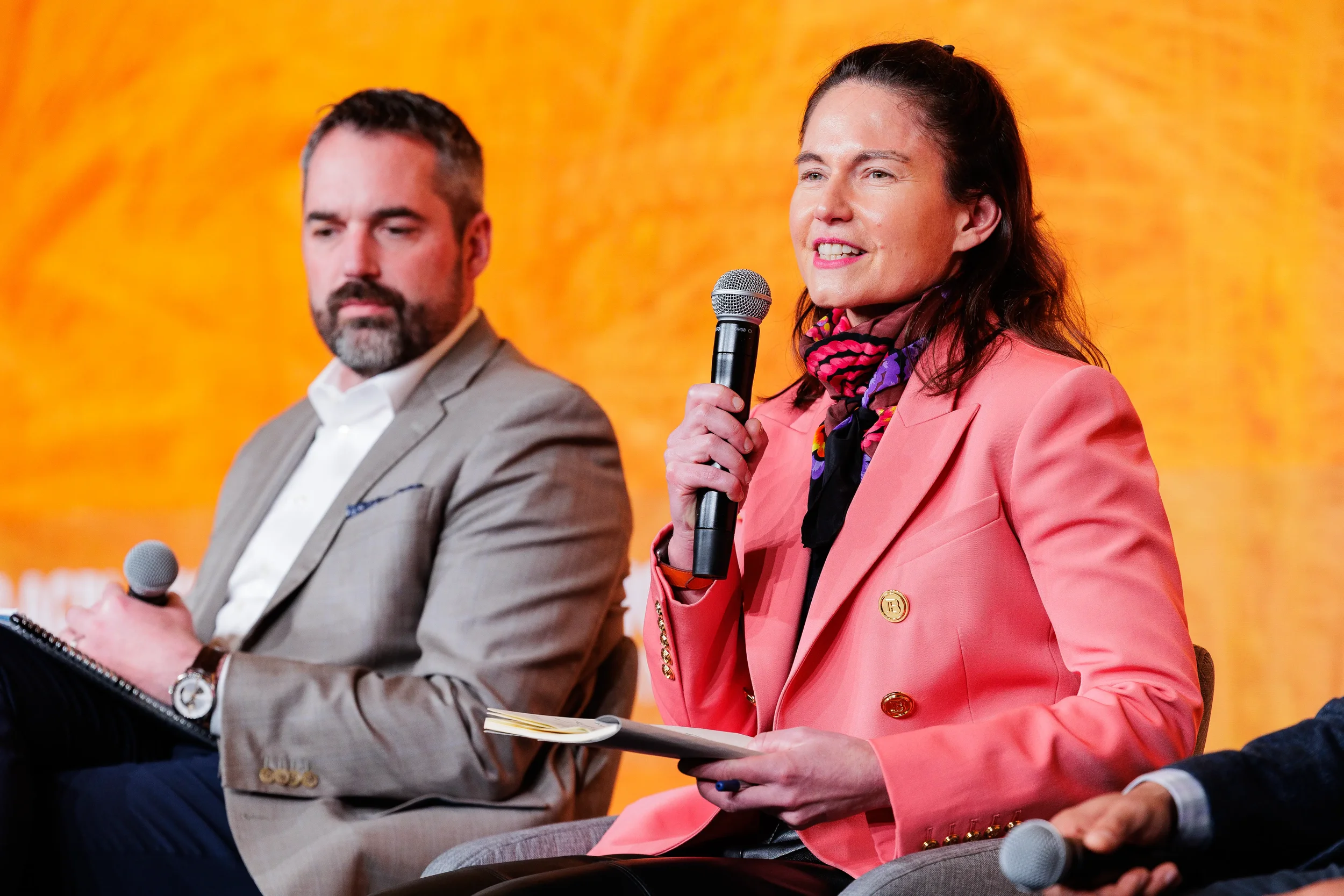Female panelist in pink blazer speaks into microphone on stage at Chicago corporate industry conference