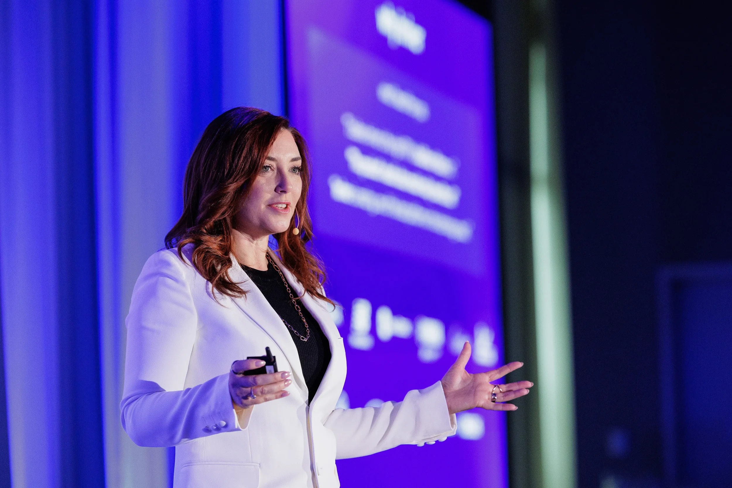 Speaker in white blazer gestures while presenting on stage at Chicago corporate conference