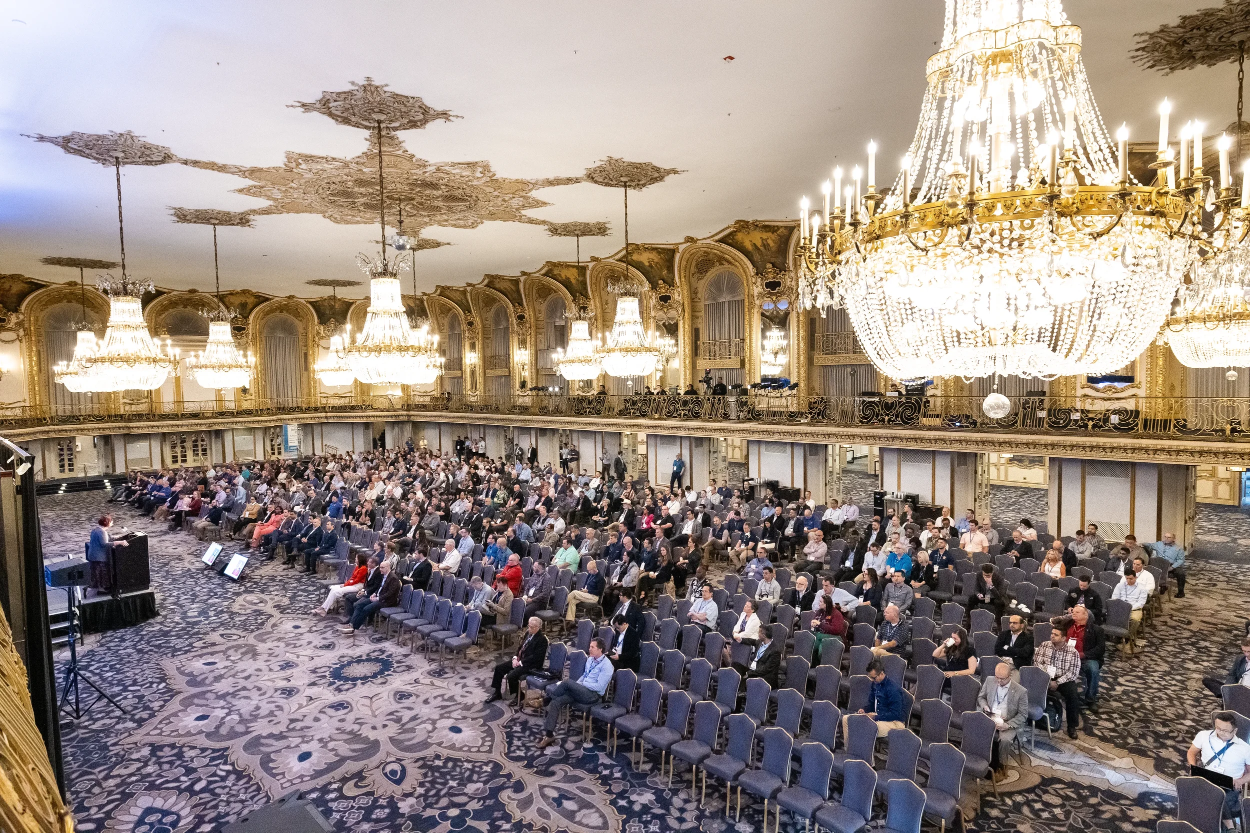 Wide view of packed audience seated in ornate ballroom at Orlando industry conference