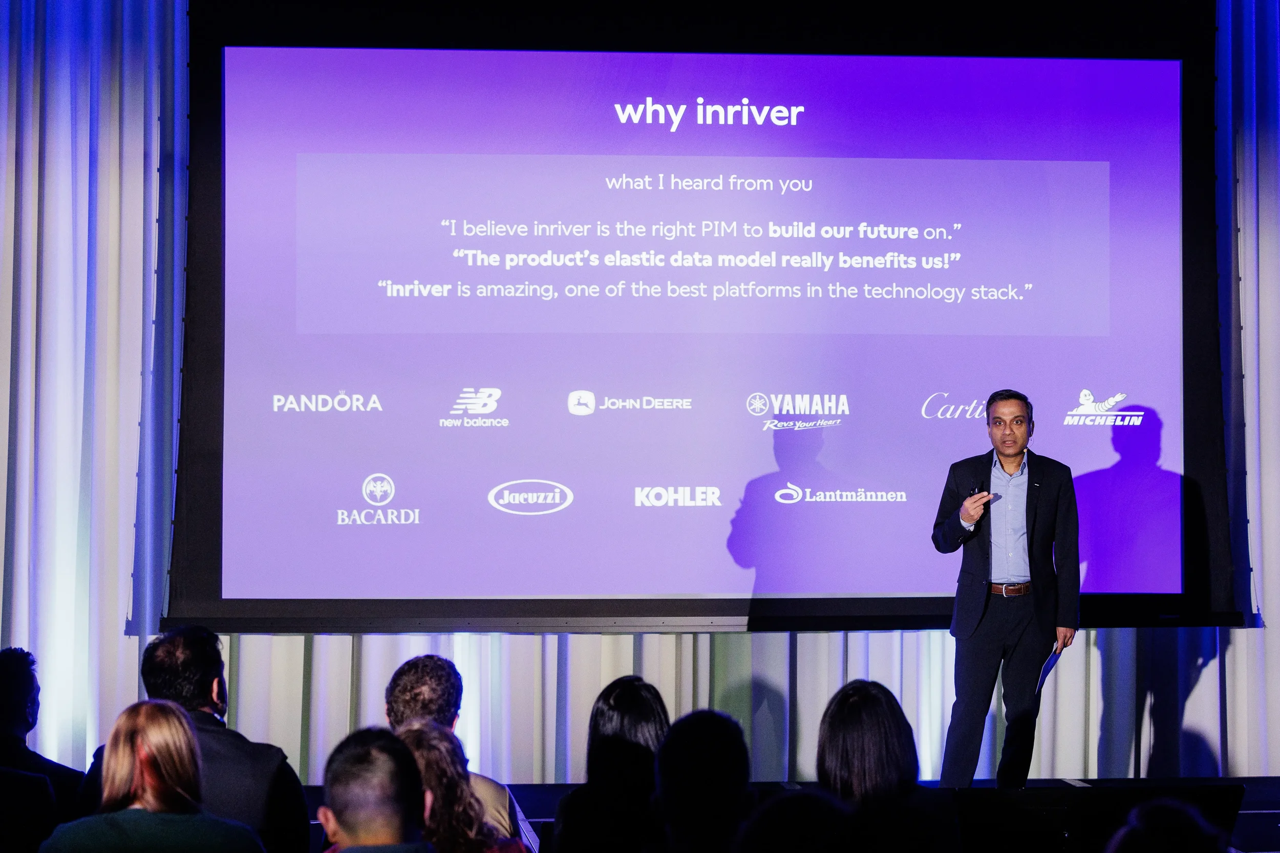 Speaker presents beside large projection screen on stage before audience at Chicago industry conference