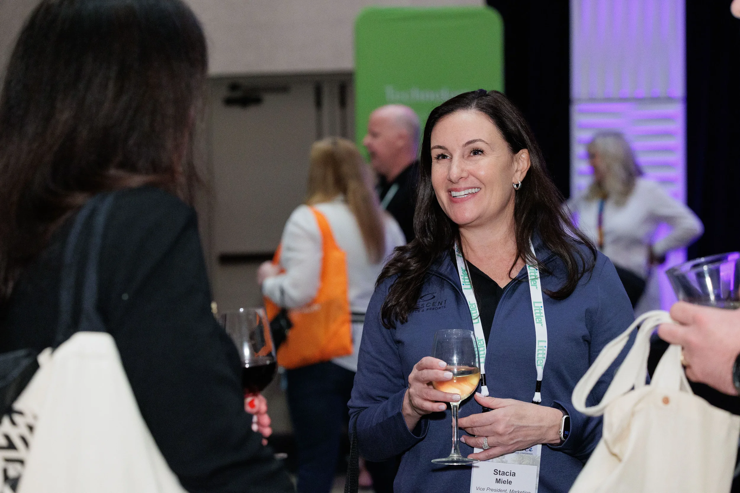 Attendee with lanyard holds wine glass and smiles during Orlando corporate conference networking reception