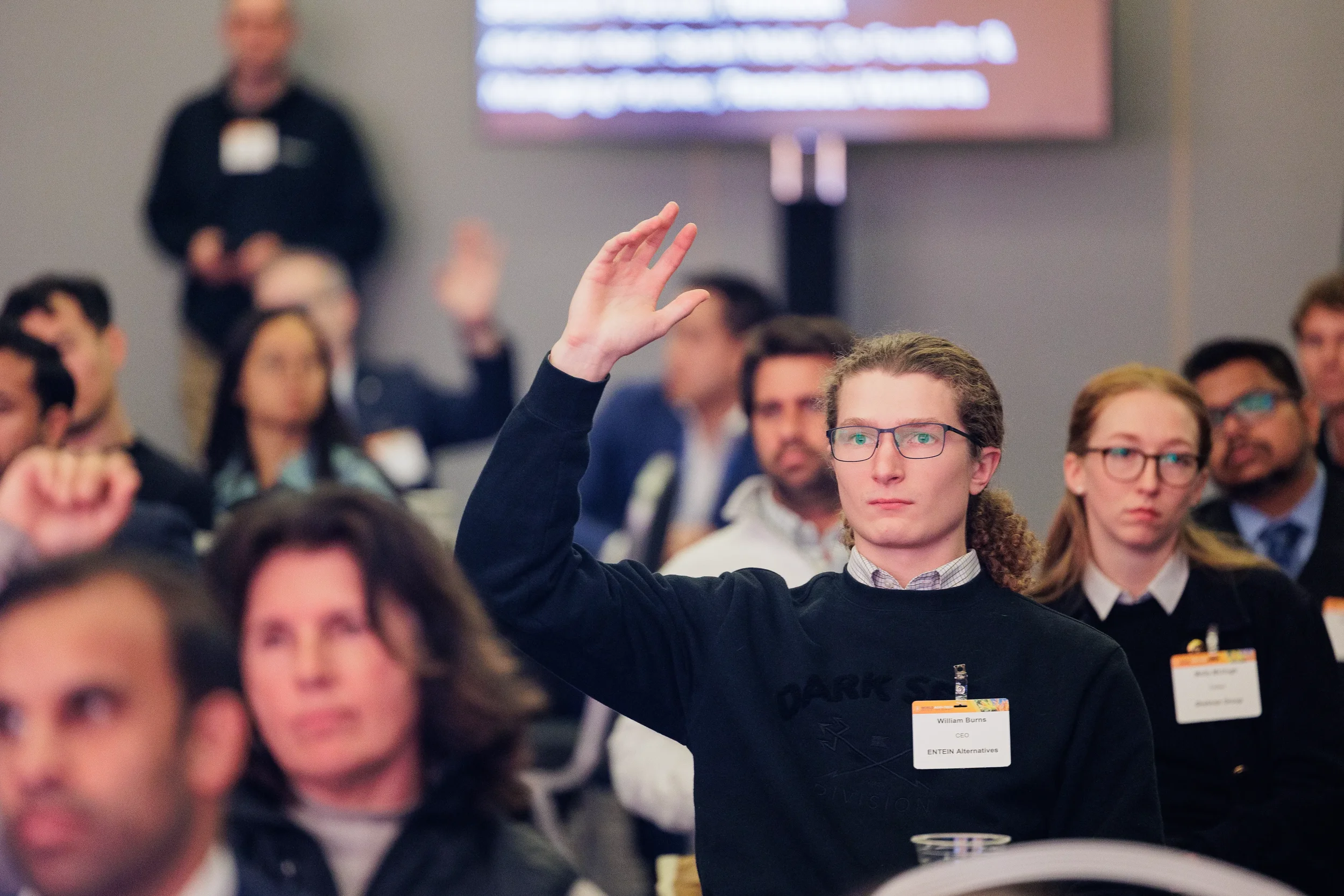 Attendee raises hand among seated audience during session at Orlando industry conference