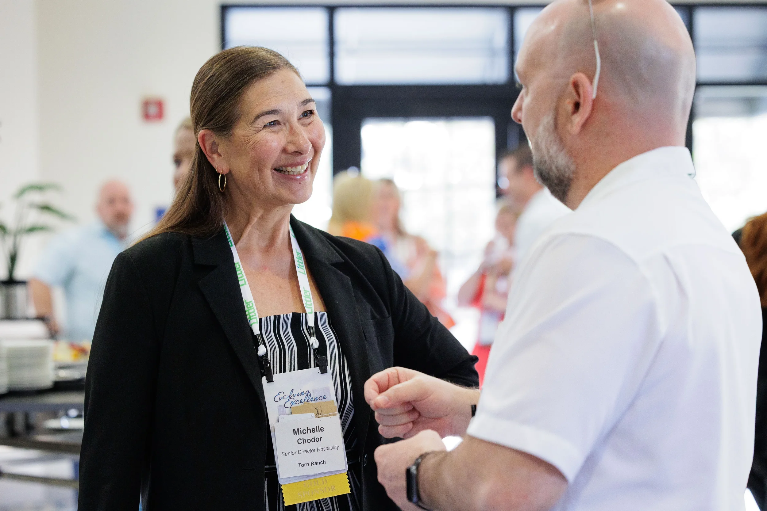 Two attendees with lanyards smile and converse during networking break at Orlando industry conference