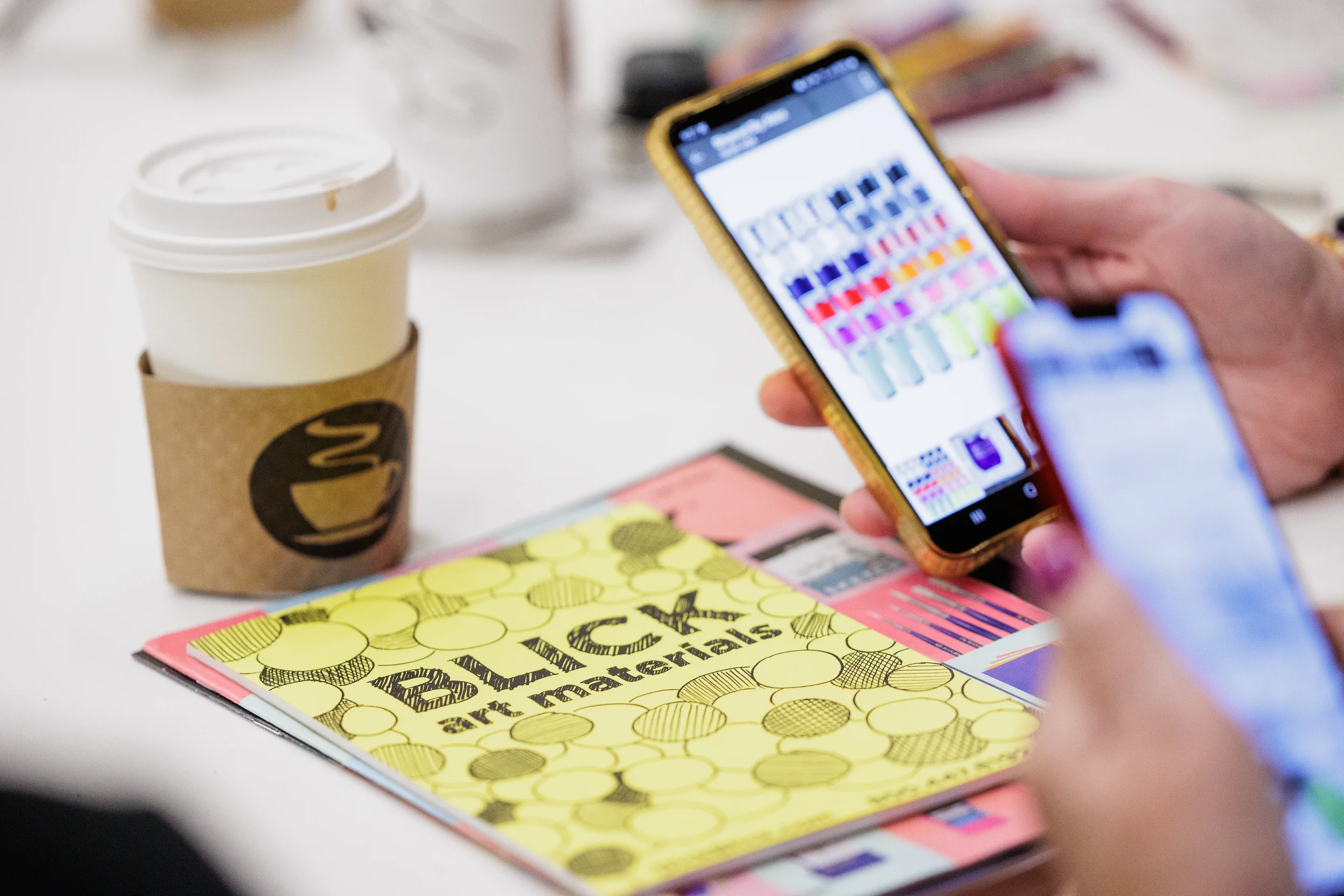 Attendee reviews color swatches on phone beside coffee and art supply catalog at Chicago conference