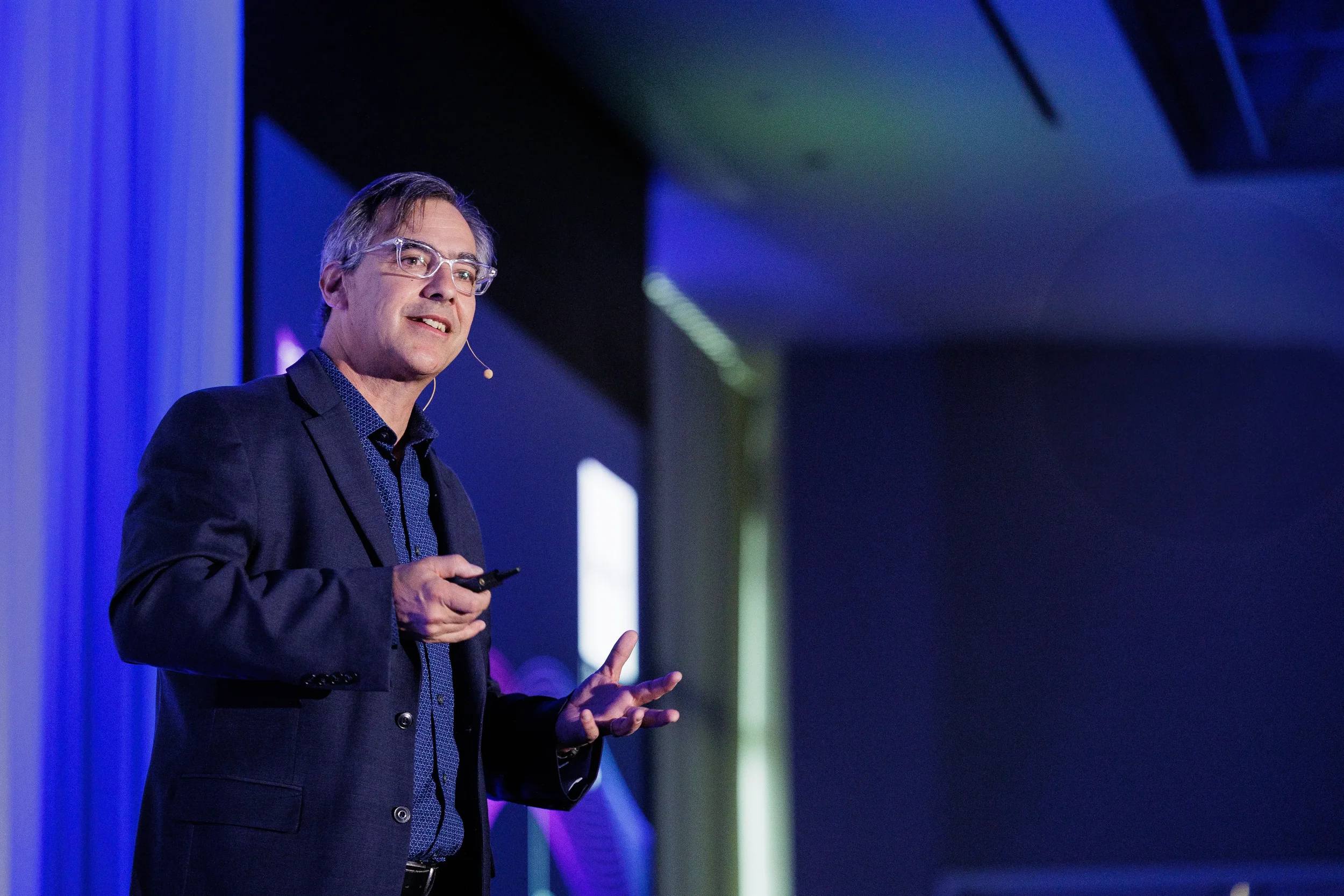 Speaker in clear glasses gestures with open hand while presenting at Chicago industry conference