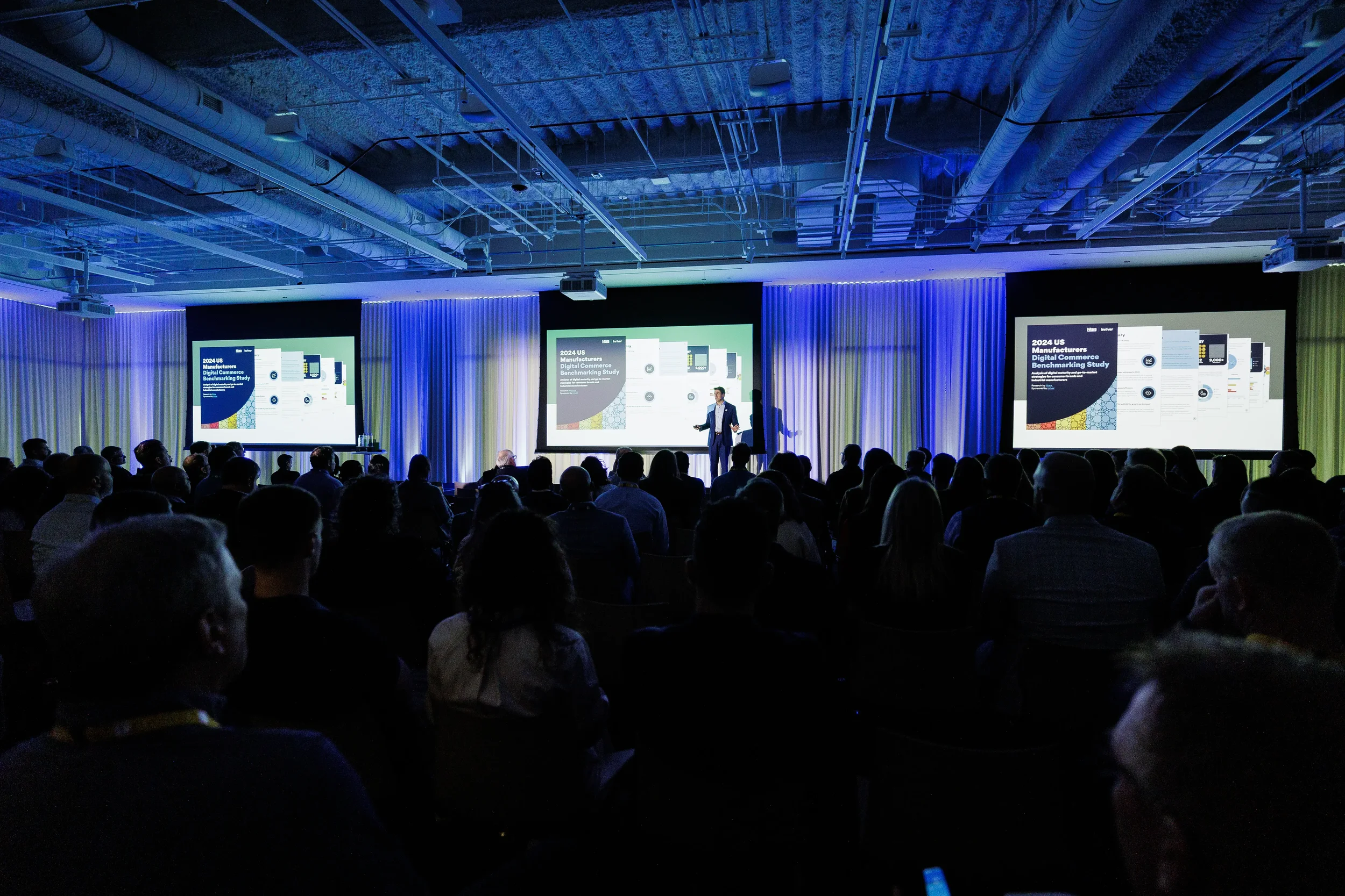 Presenter speaks before three projection screens as audience watches in blue-lit Orlando industry conference