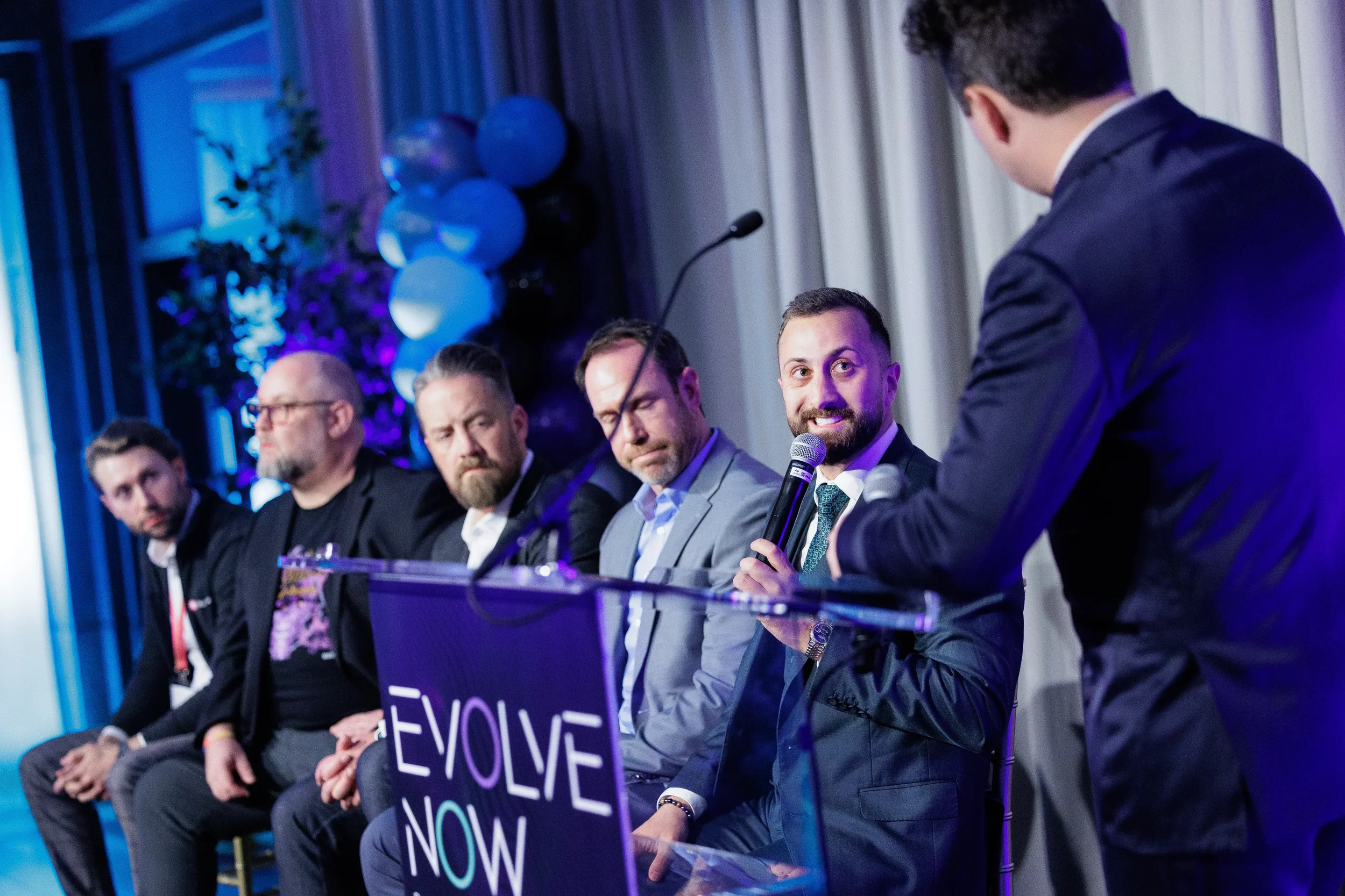 Panelist speaks at podium beside seated panel while moderator looks on at Orlando industry conference