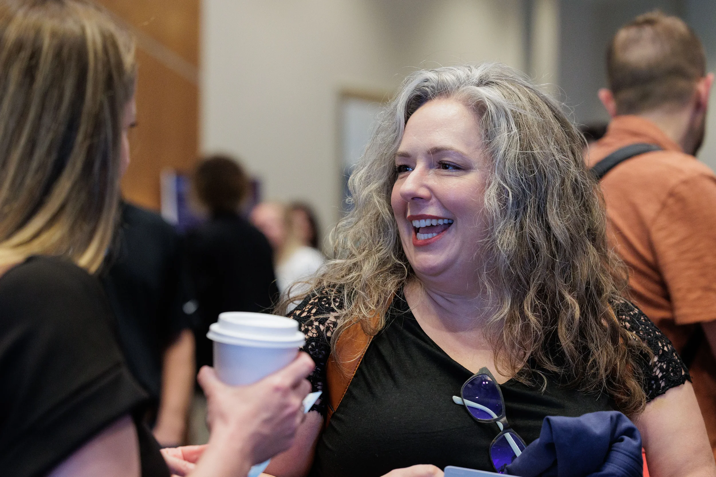 Smiling attendee holds coffee cup while laughing during networking reception at Chicago industry conference