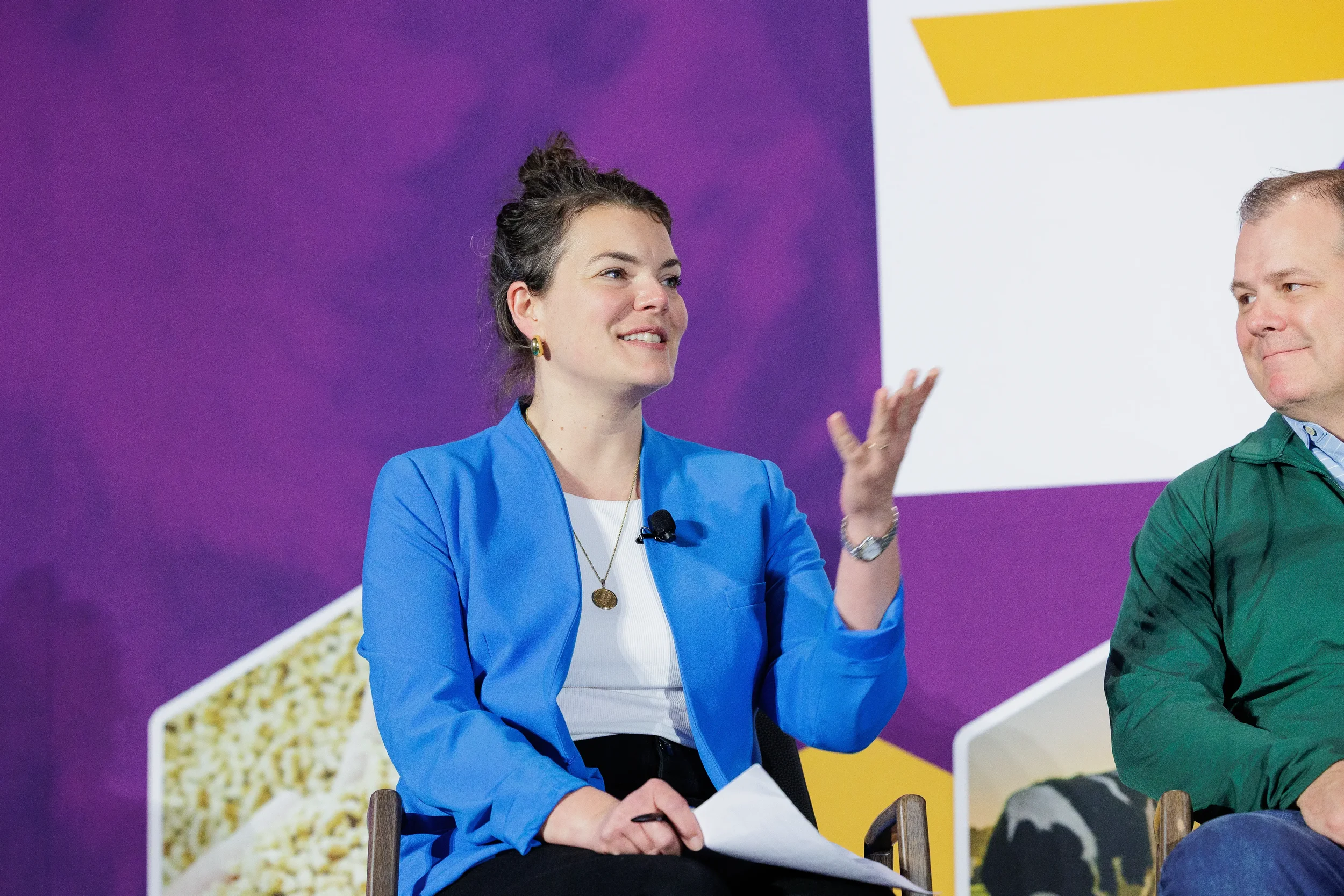 Speaker in blue blazer gestures while presenting on branded stage at Orlando industry summit