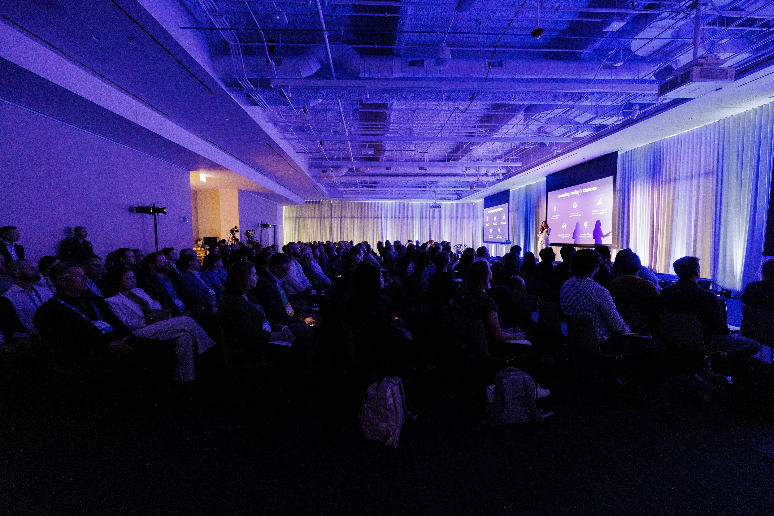 Packed audience watches keynote presentation in purple-lit ballroom at Chicago industry conference