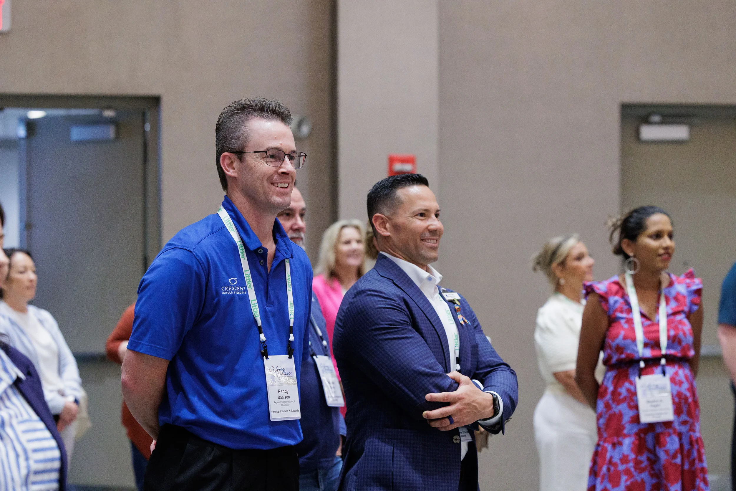 Two attendees with lanyards smile while watching activity in ballroom at Chicago industry conference