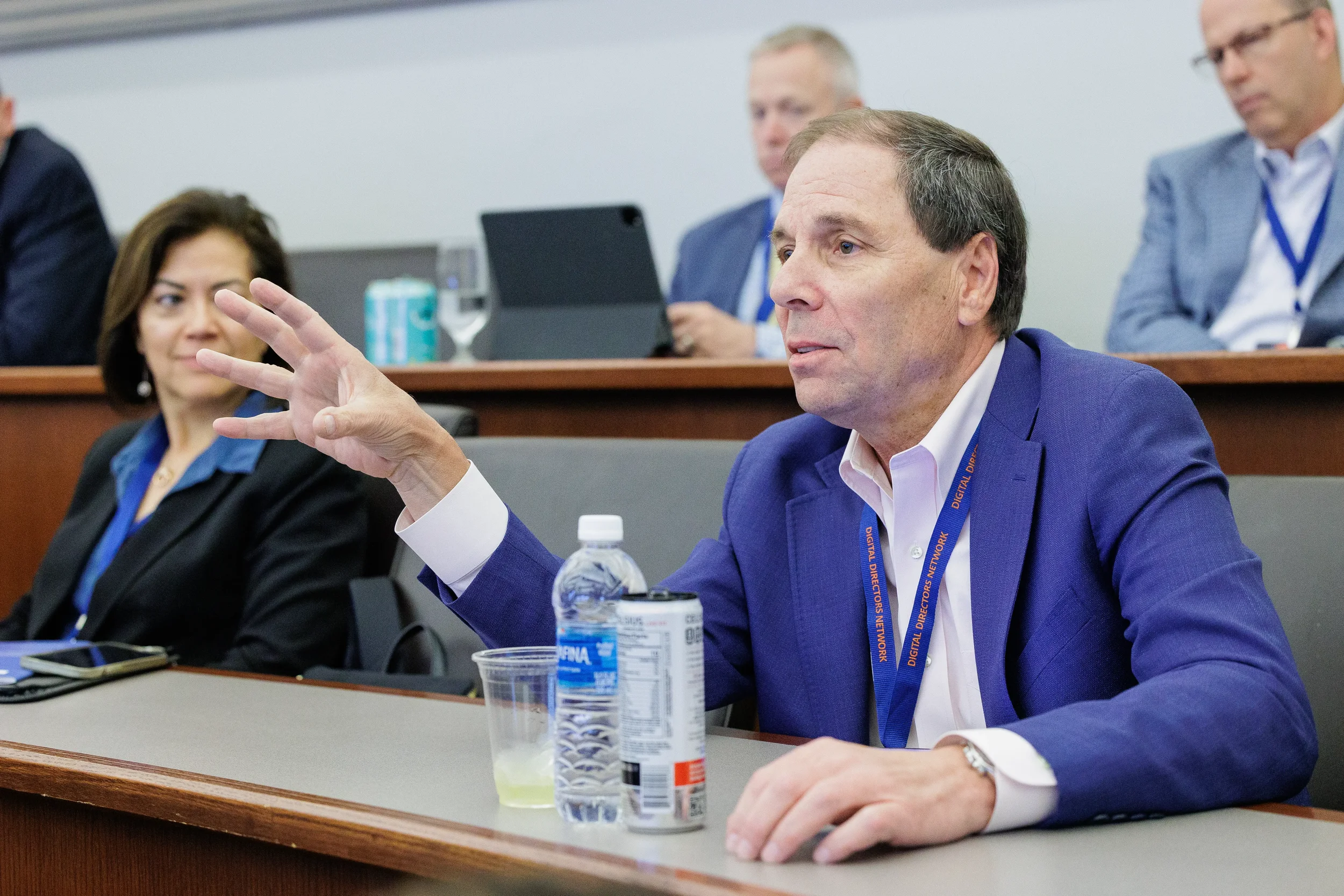 Male attendee with lanyard raises hand while seated in tiered room at Chicago corporate conference session