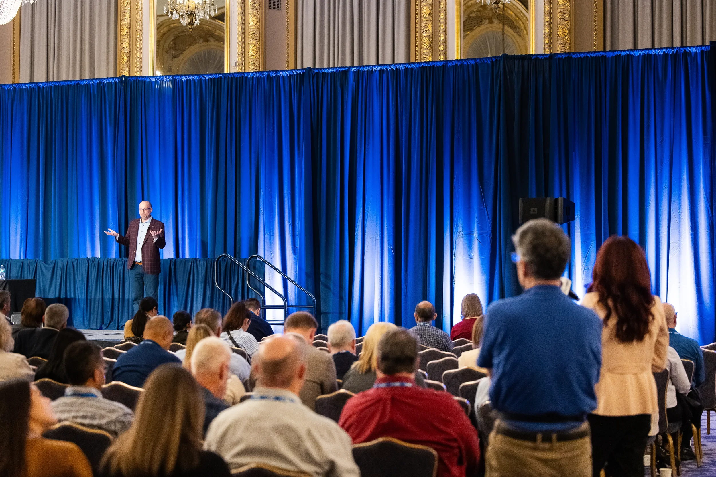 Keynote speaker gestures on stage before packed ballroom audience at Orlando conference