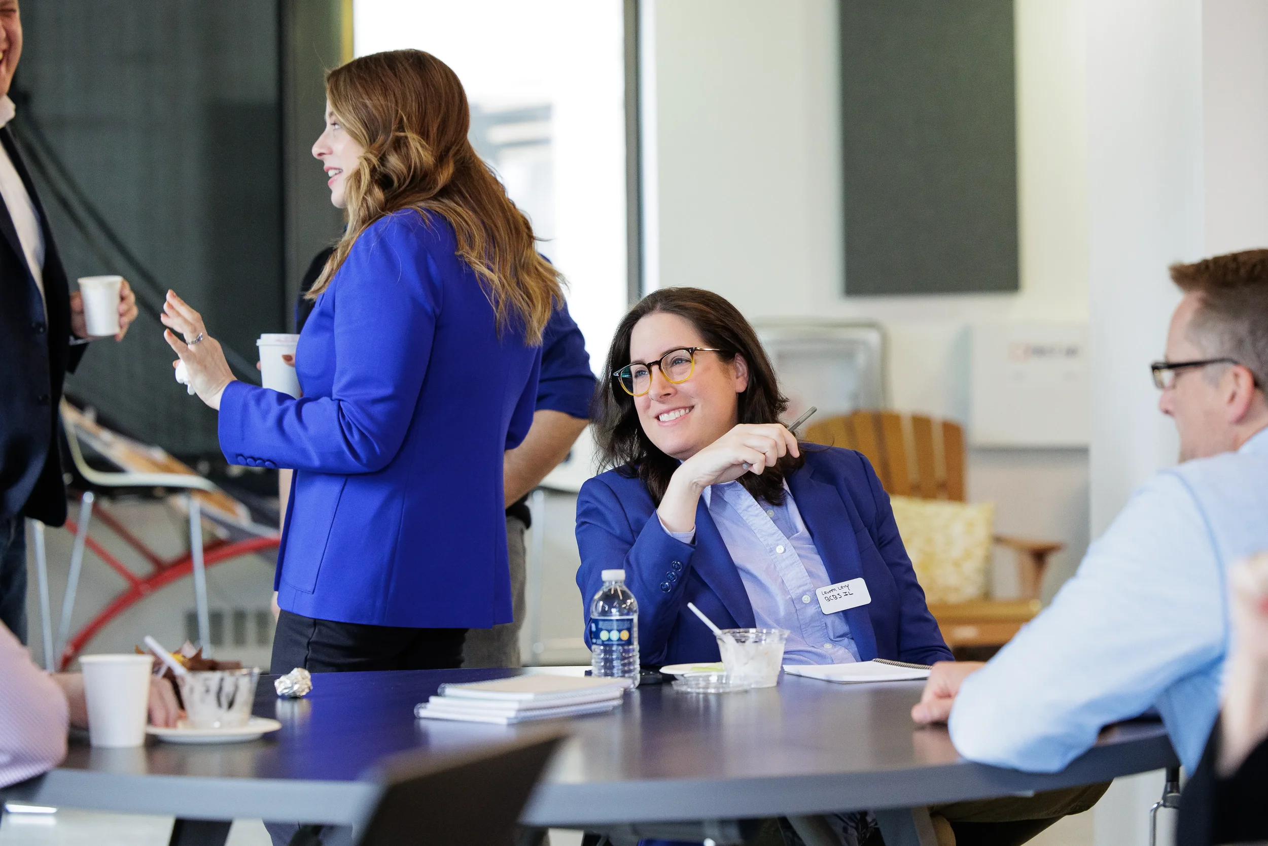 Attendee smiles at table during Chicago corporate event session while colleagues chat nearby
