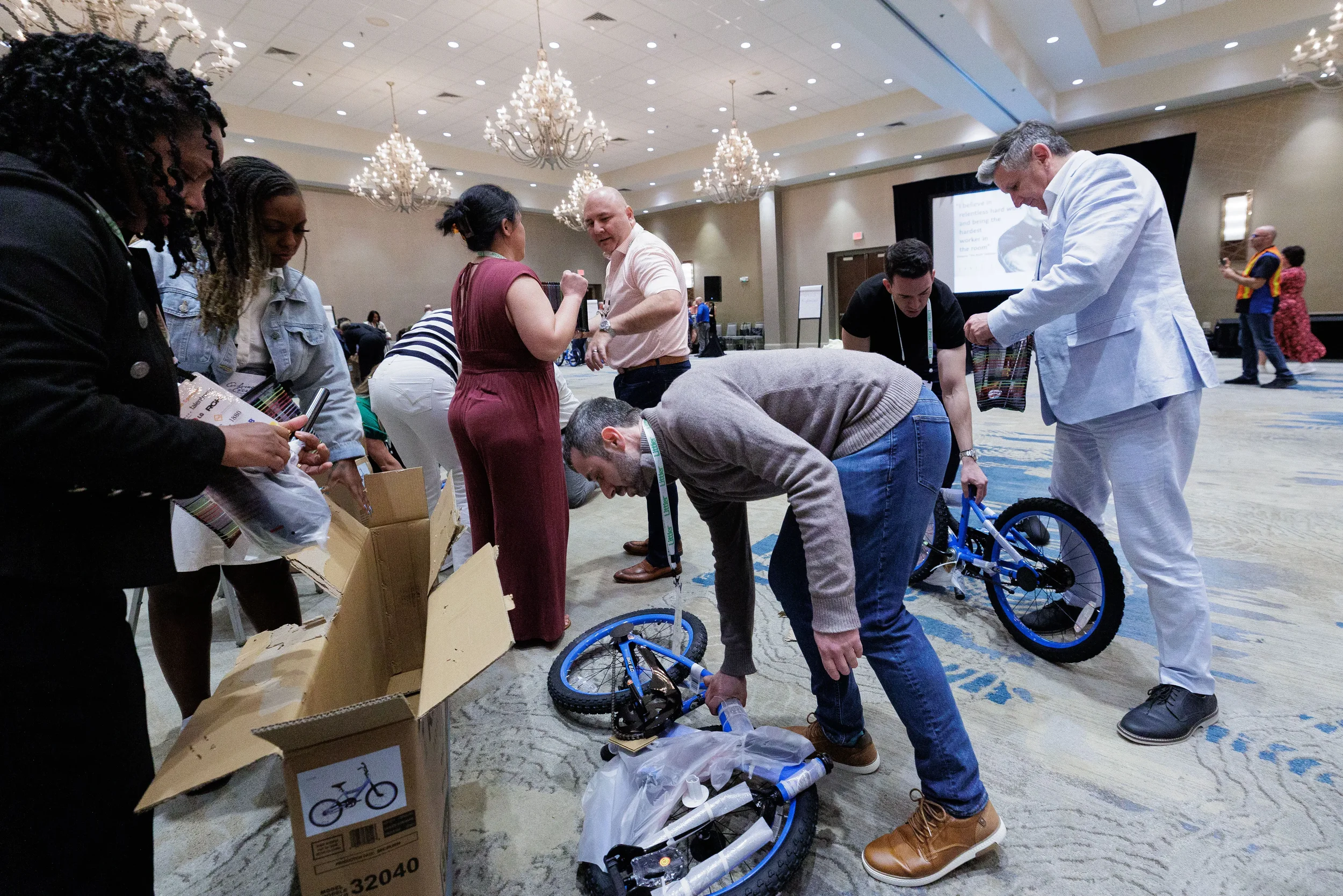 Attendees work together assembling bicycles from boxes in chandelier ballroom at Orlando corporate event