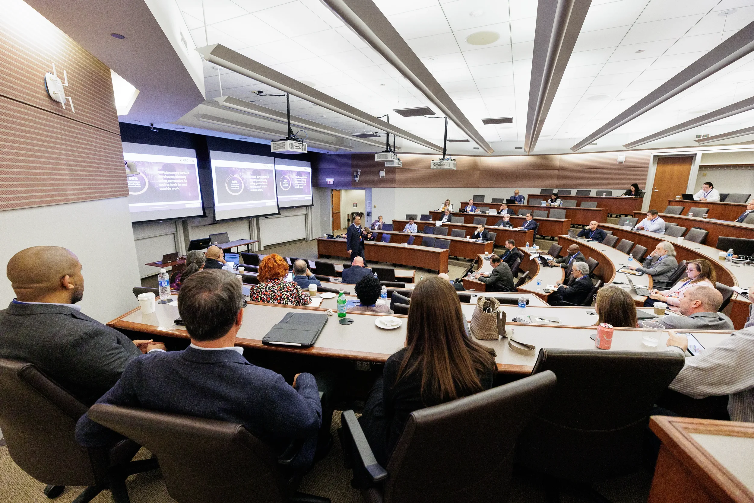 Speaker presents to full tiered lecture hall with dual projection screens at Orlando industry conference