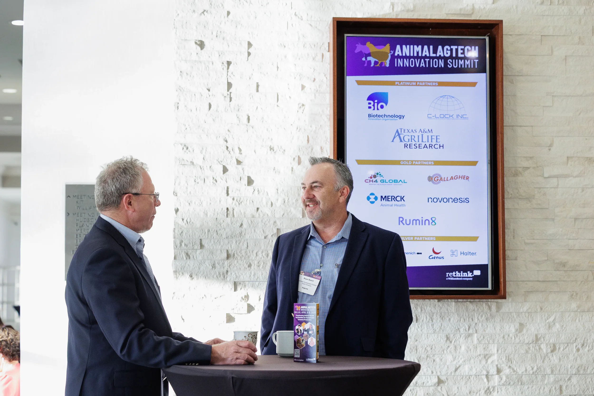 Two attendees converse near sponsor signage display at Chicago corporate conference