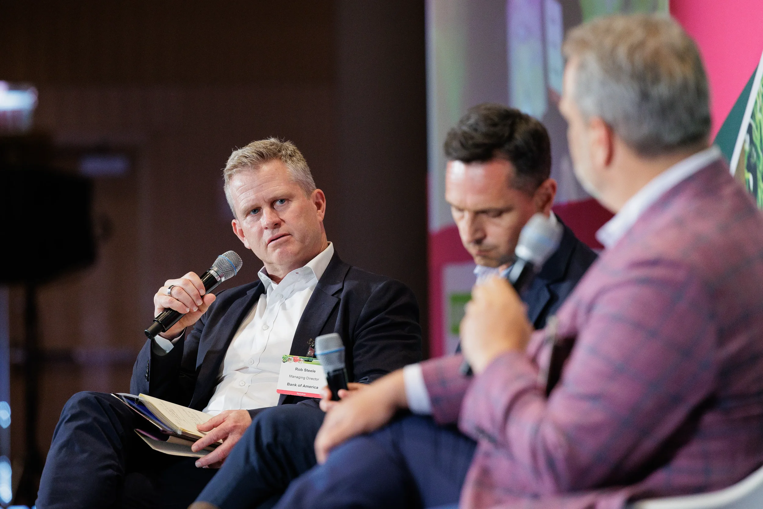 Panelist speaks into handheld microphone while fellow speakers listen on stage at Orlando conference