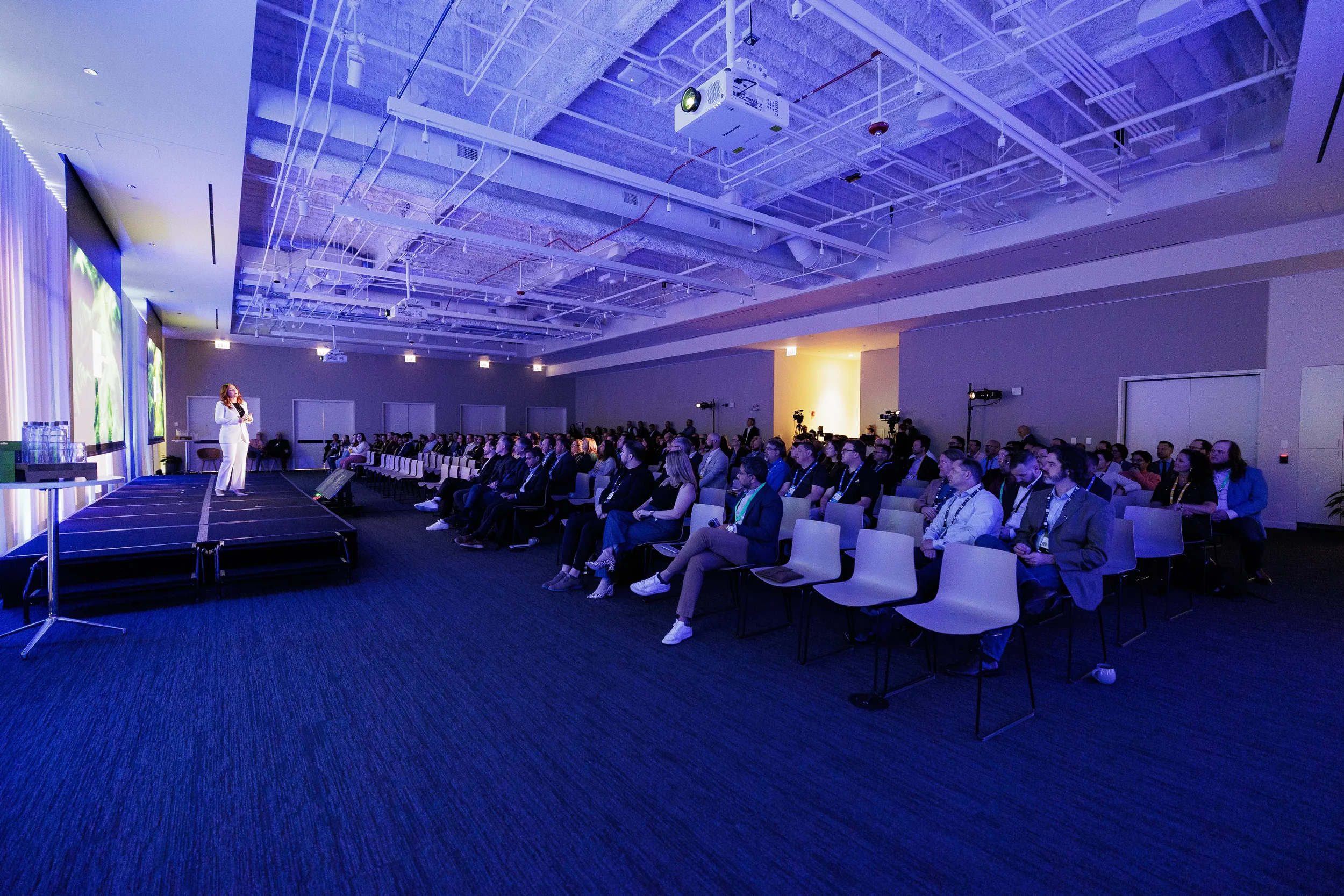 Wide view of speaker on stage before seated audience in blue-lit room at Chicago corporate conference