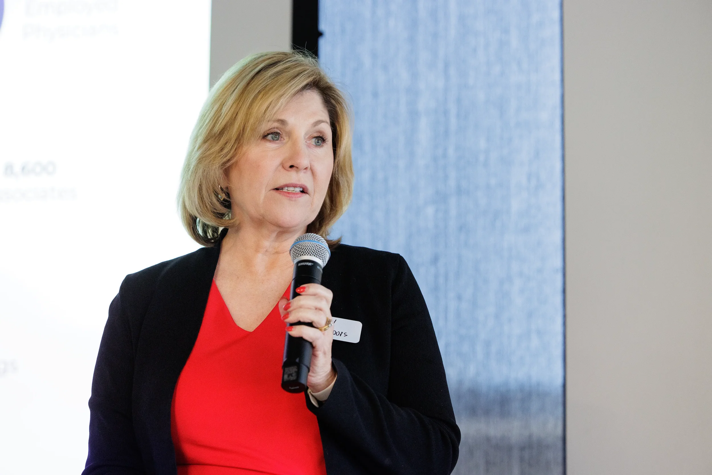 Female speaker presents with handheld microphone beside projected slides at Chicago industry conference