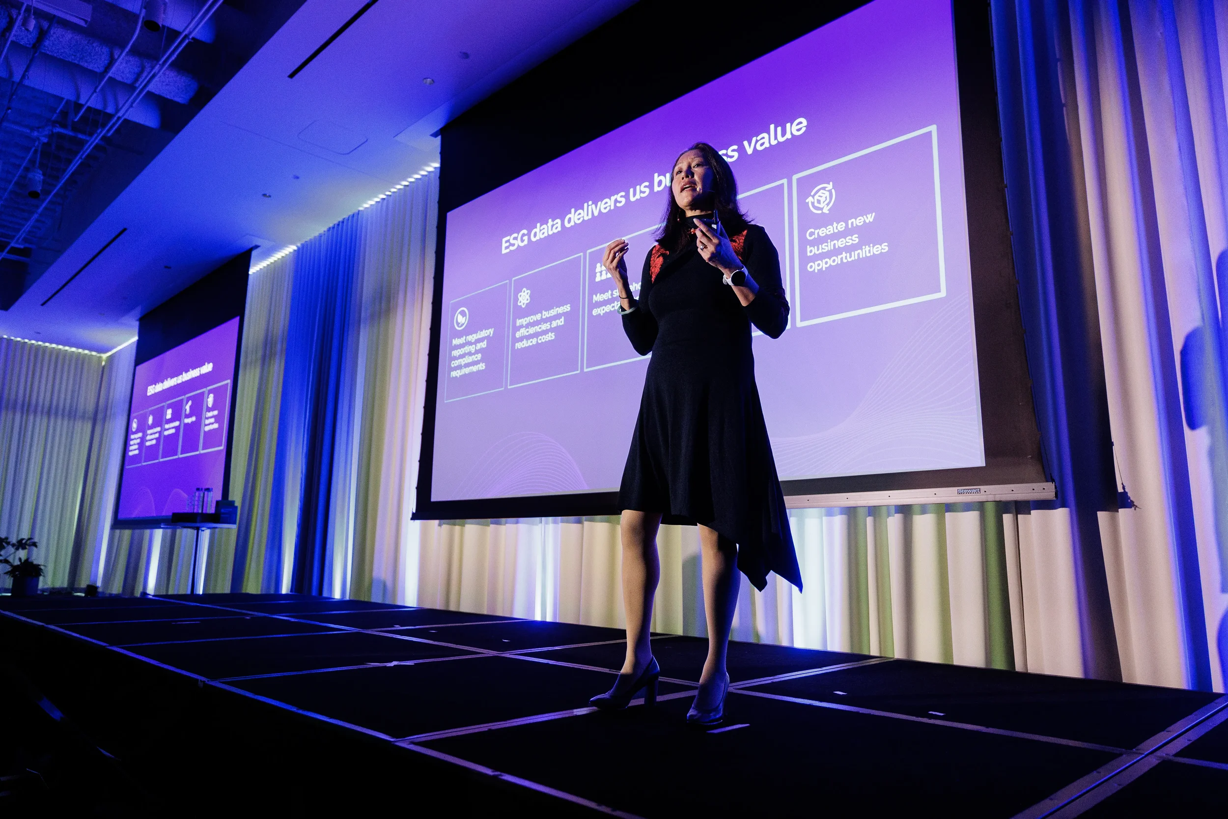 Speaker gestures on stage in front of purple business value slide at Chicago industry conference