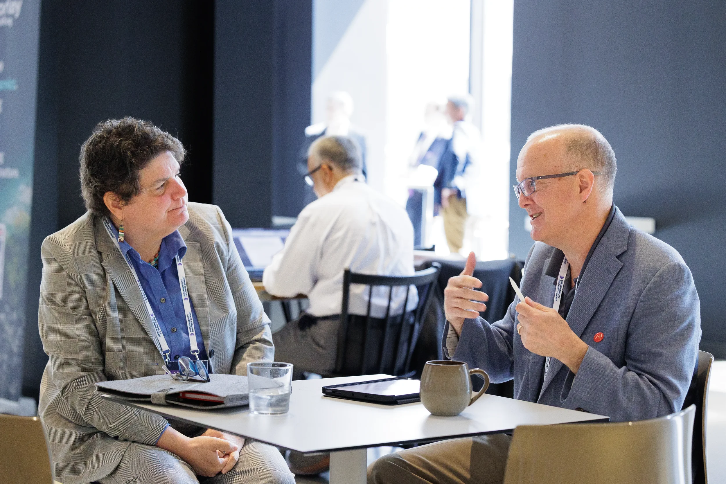 Two attendees converse over coffee at seated table during Orlando corporate conference break