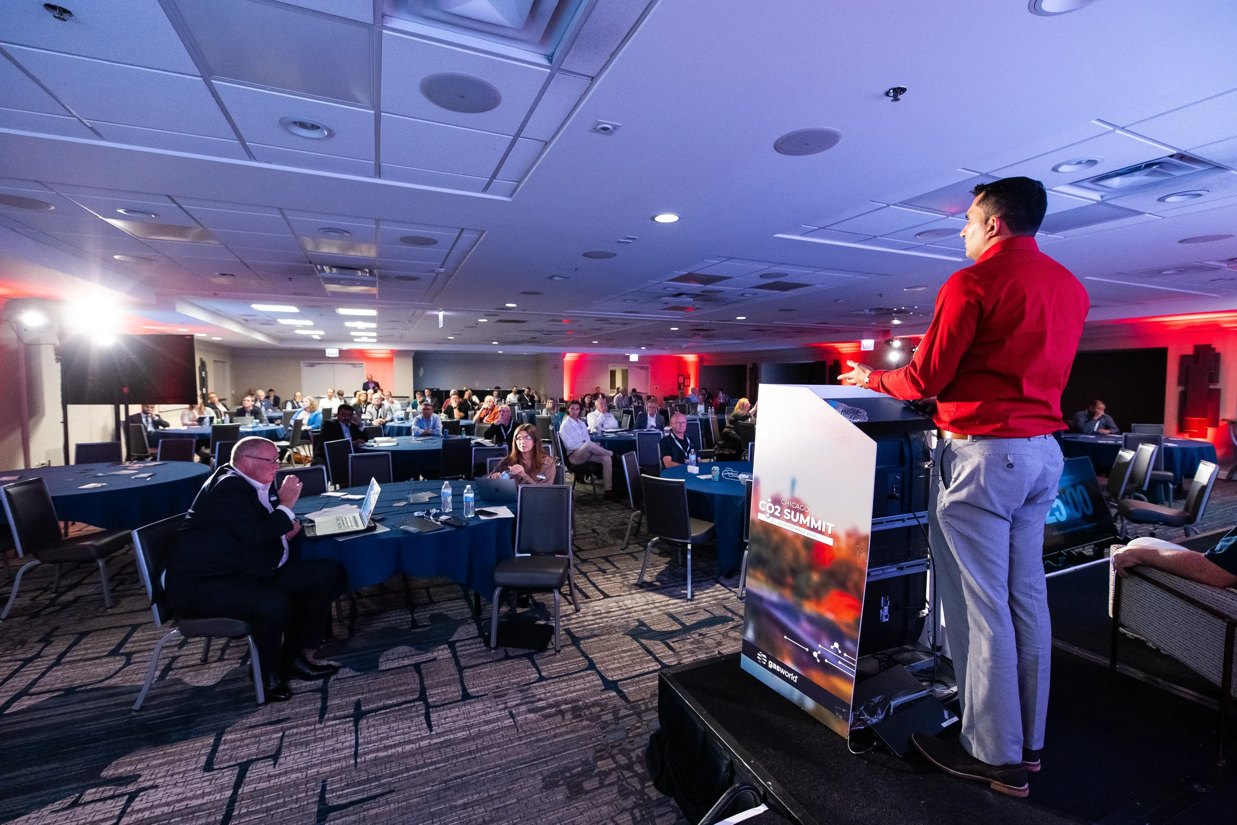 Speaker gestures from podium while addressing seated audience in Orlando conference ballroom