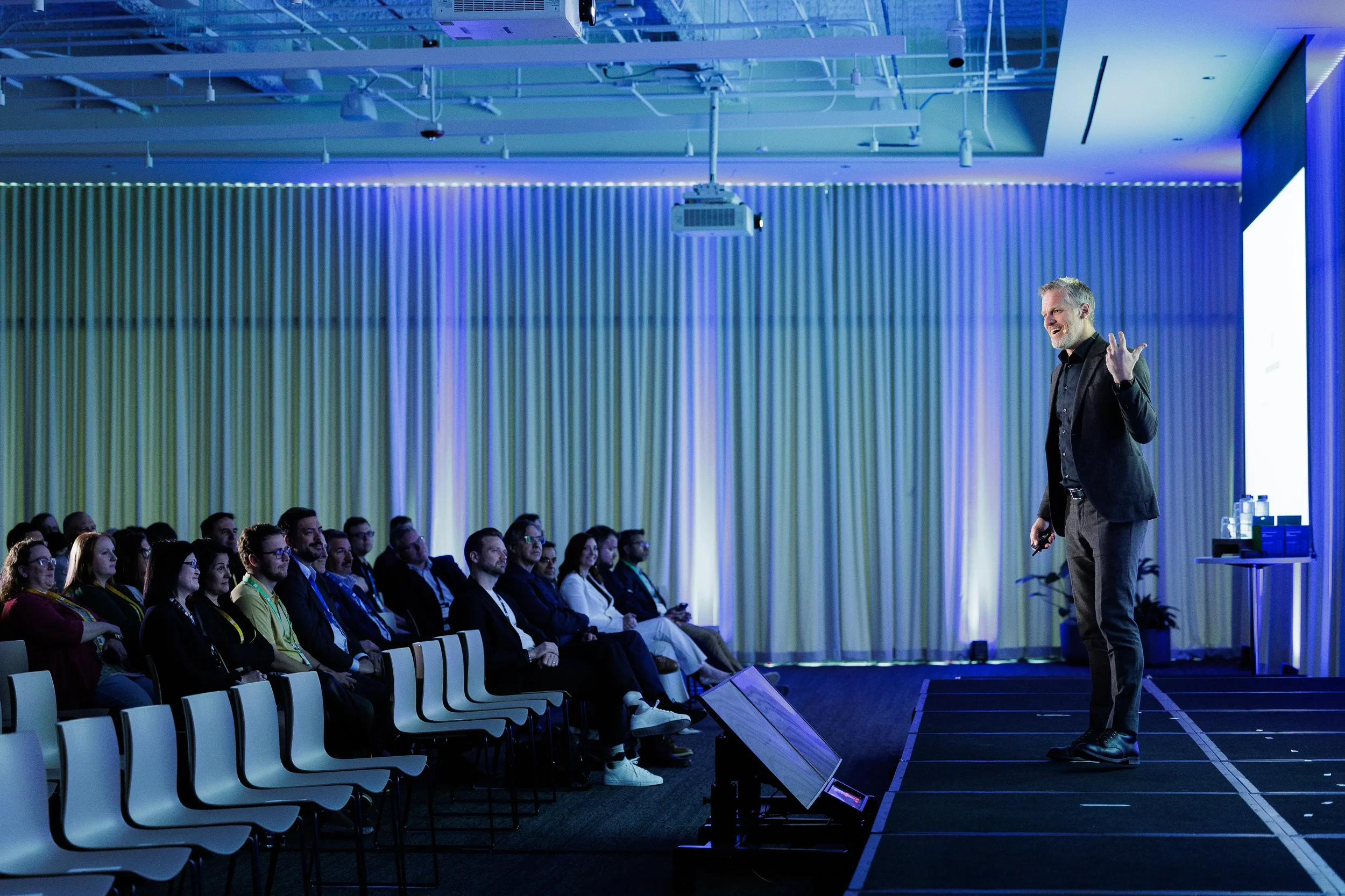 Speaker smiles and gestures on stage as seated audience listens at Orlando corporate conference