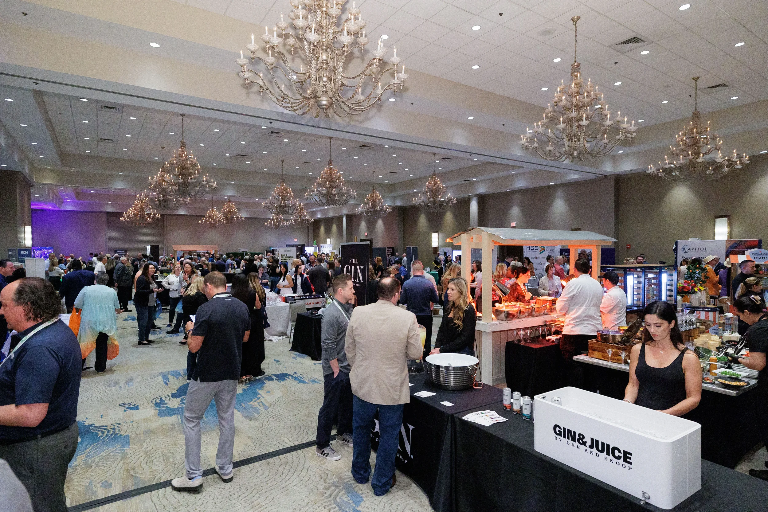 Packed expo floor with attendees browsing exhibitor booths in chandelier ballroom at Orlando corporate conference