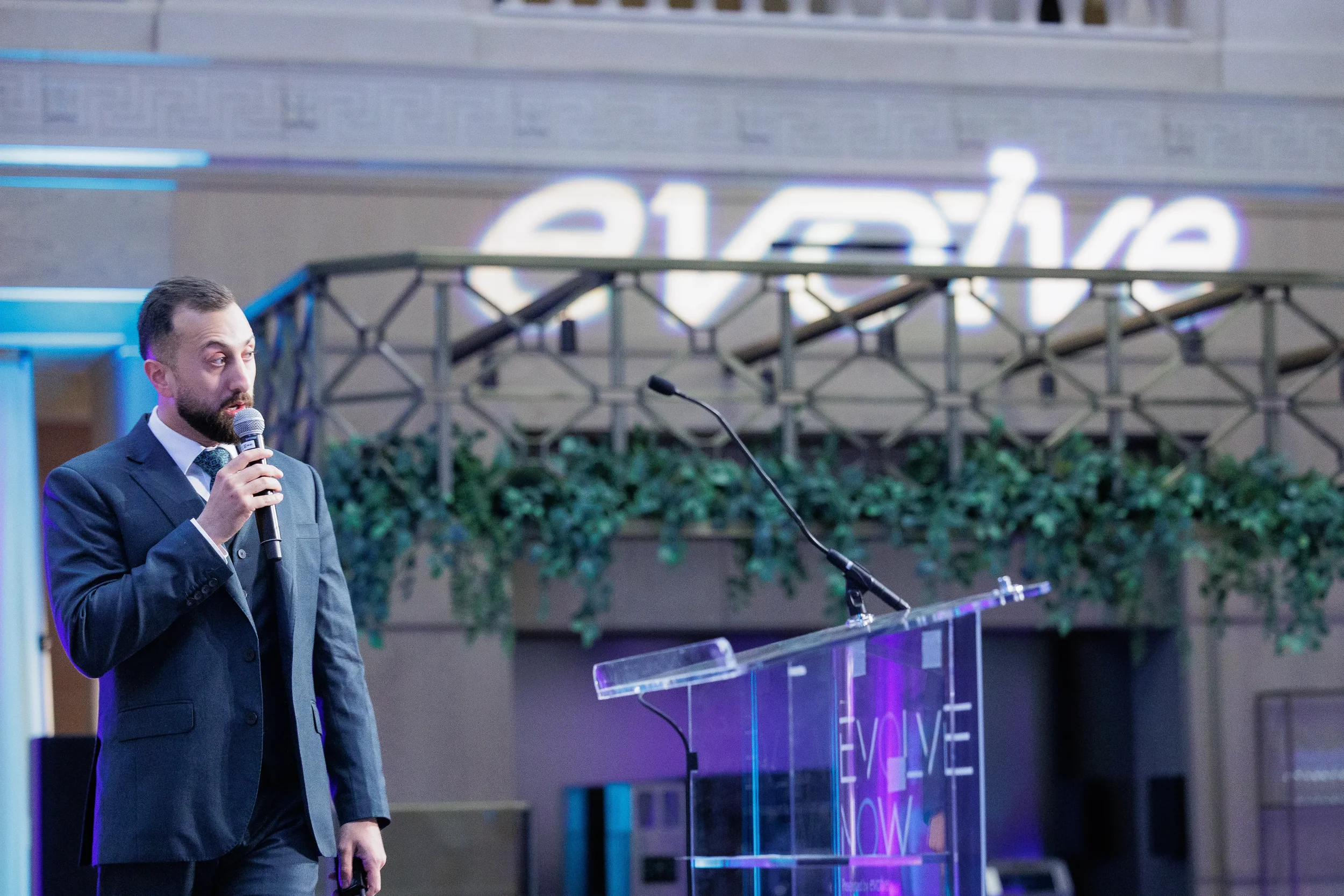 Speaker addresses audience at podium with glowing brand sign in atrium at Orlando corporate event