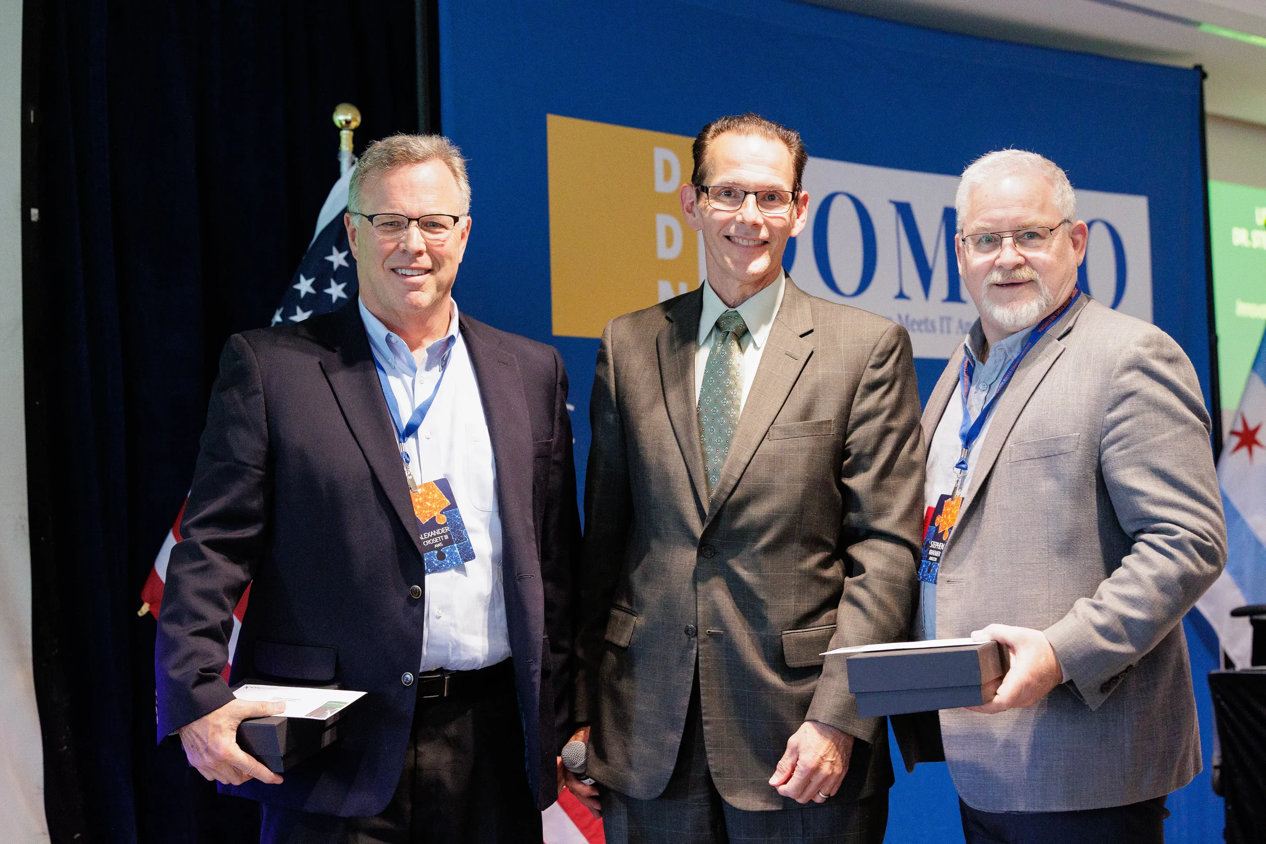 Three male attendees with lanyards pose together in front of branded backdrop at Orlando corporate event
