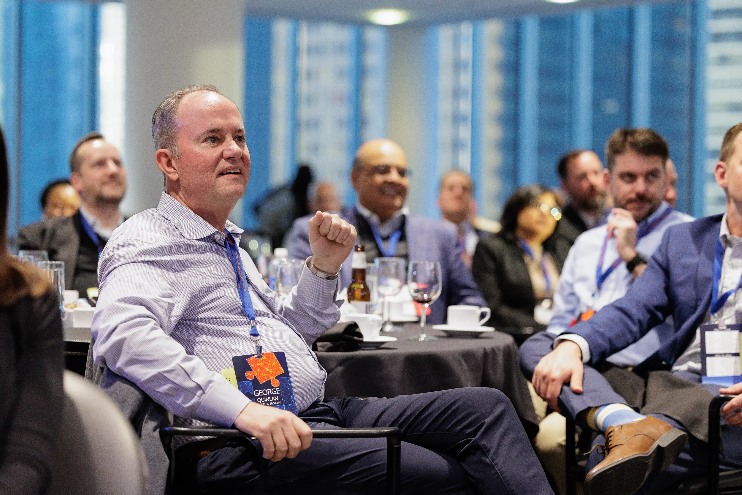Male attendee with lanyard gestures while seated at round table during Chicago industry conference session