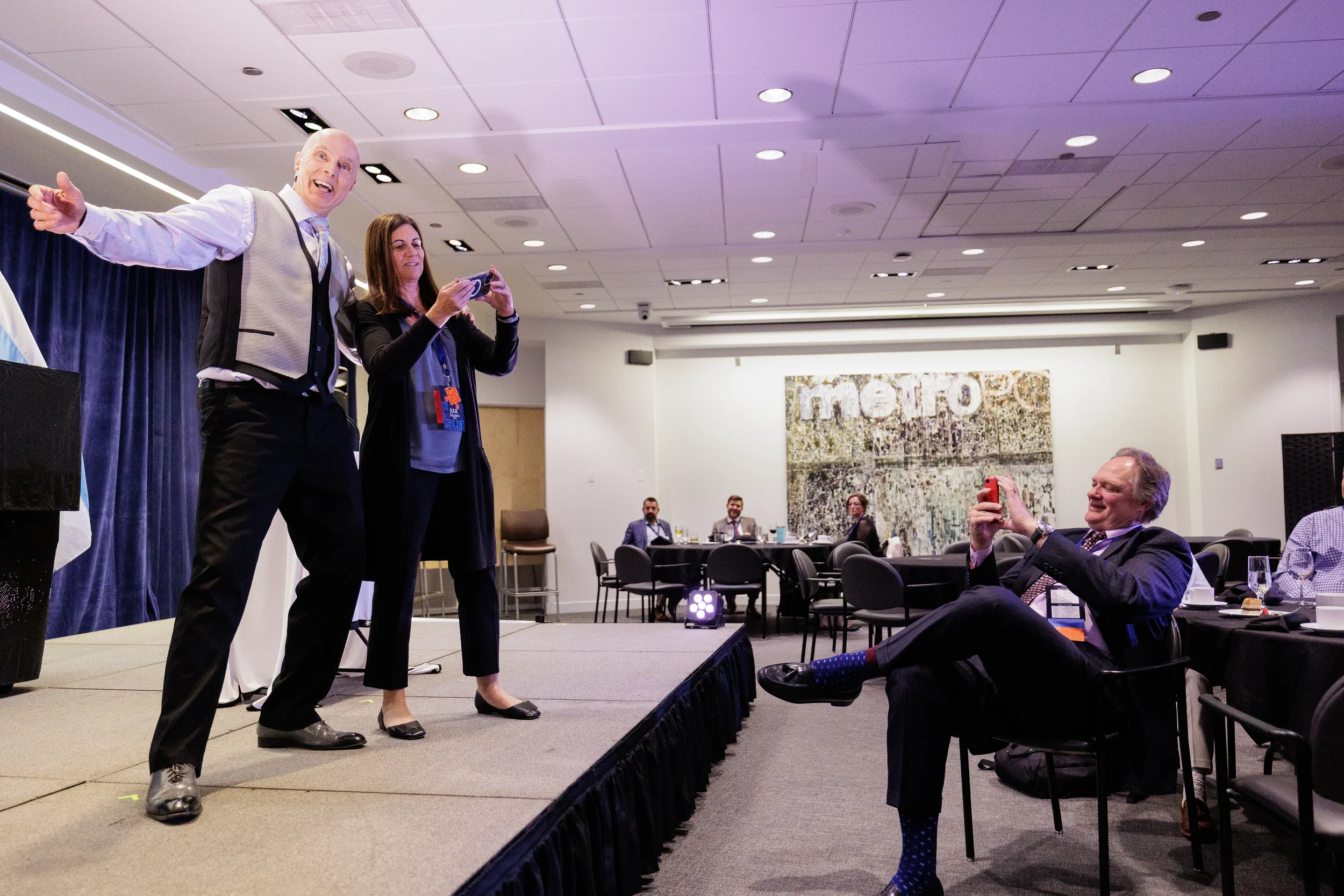 Entertainer spreads arms on stage while female attendee photographs him at Orlando corporate conference event