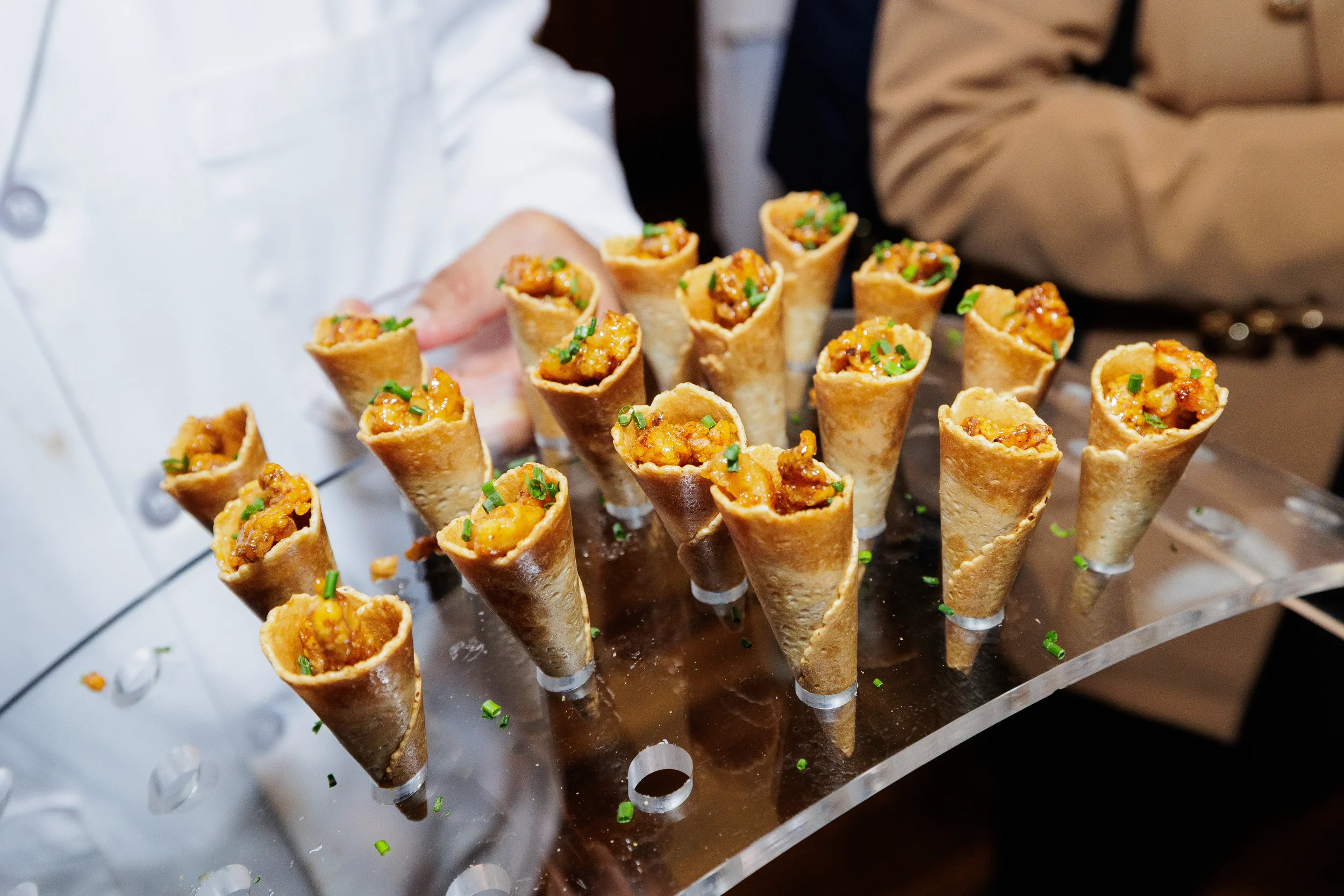 Clear acrylic tray holding small waffle cones filled with orange-glazed shrimp and topped with chopped chives in Orlando