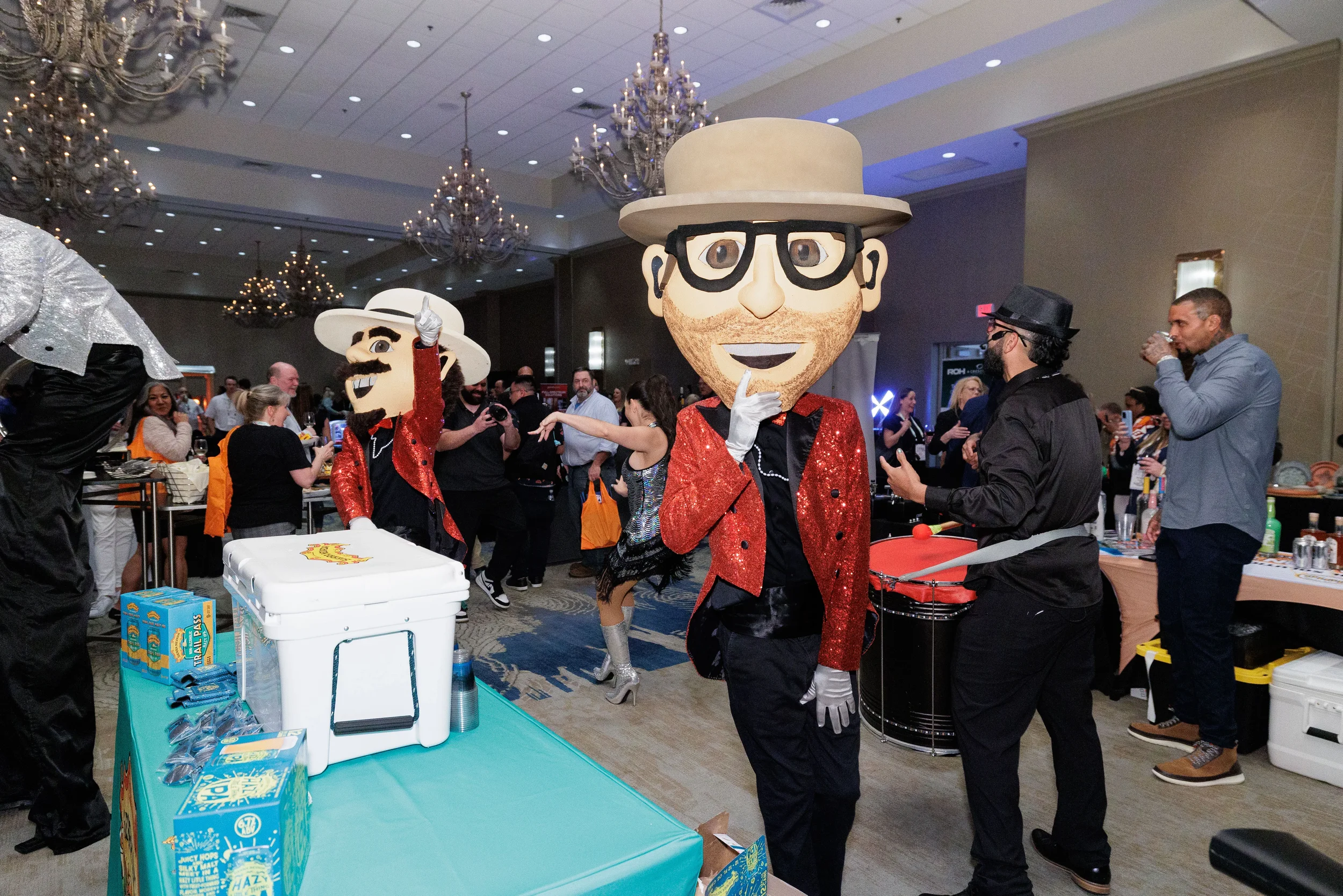 Two oversized mascot characters in red sequin jackets perform on expo floor at Chicago corporate conference