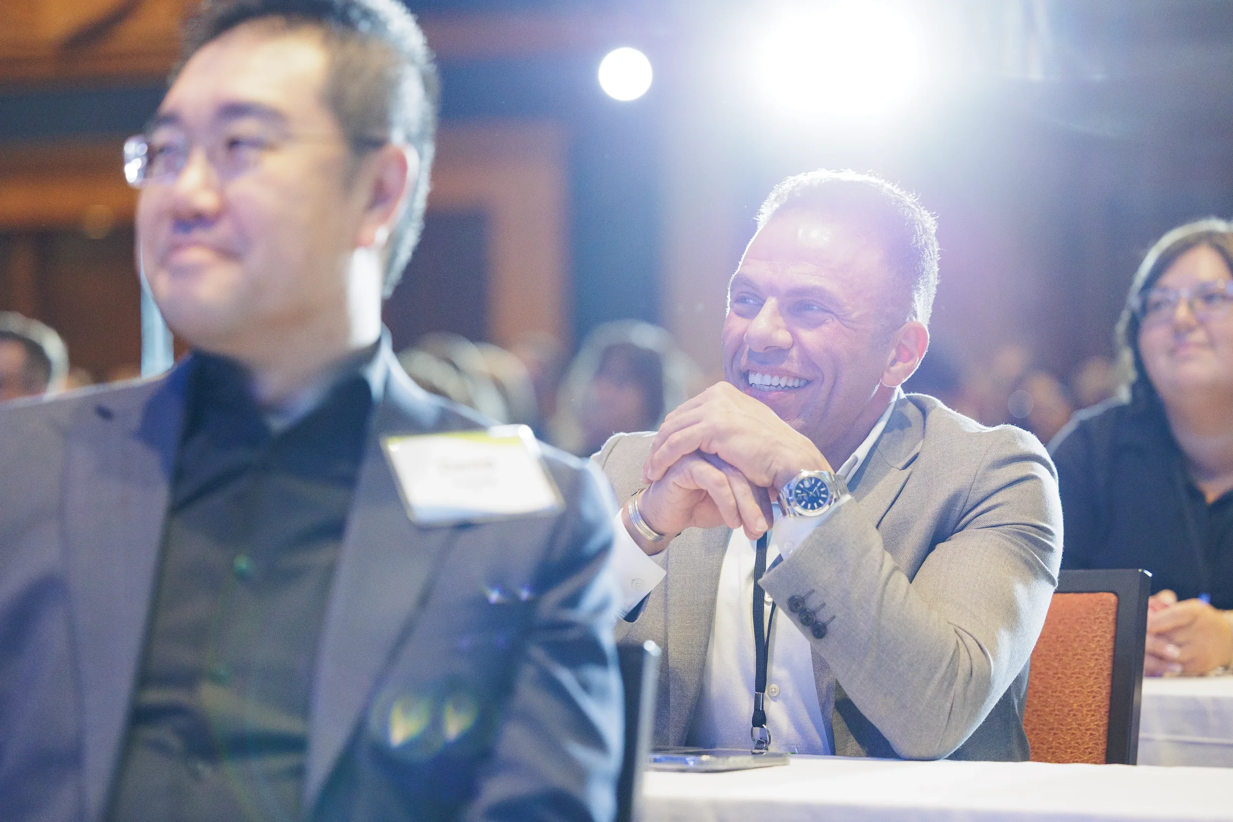 Smiling attendee rests chin on clasped hands in backlit audience at Orlando corporate summit