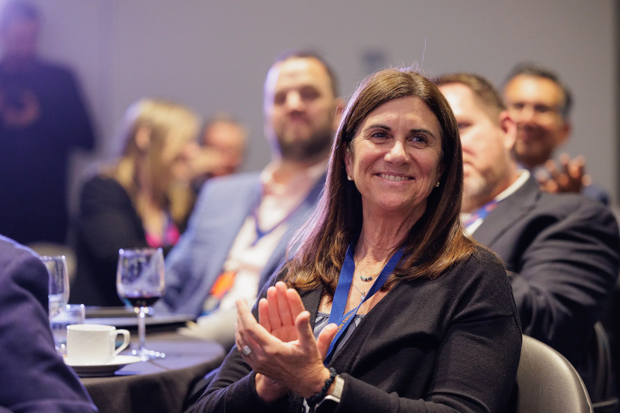 Smiling female attendee with lanyard claps while seated during Chicago corporate conference event program