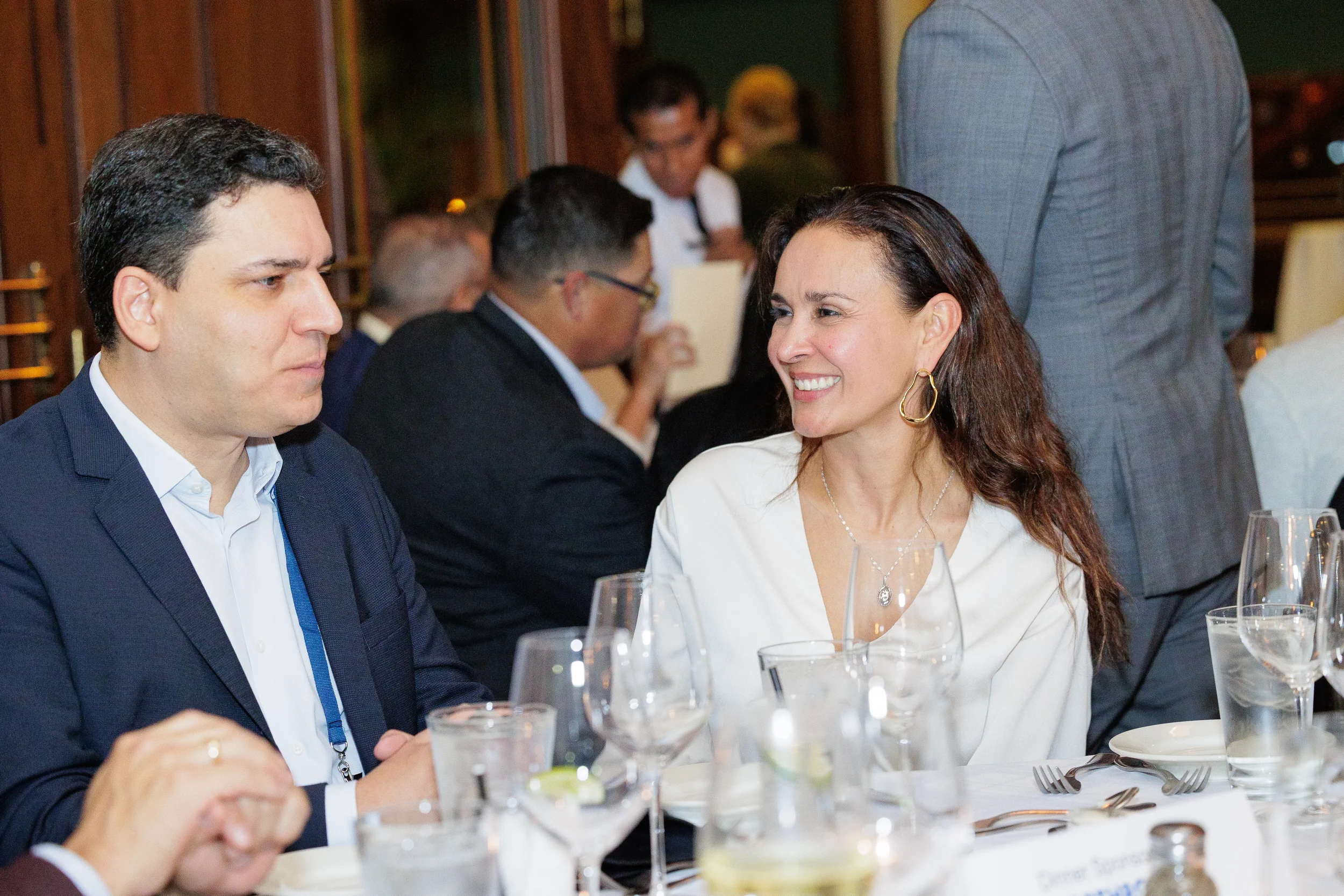 A man in a dark suit and a smiling woman in a white top sit at a dinner table with multiple wine glasses in Chicago.