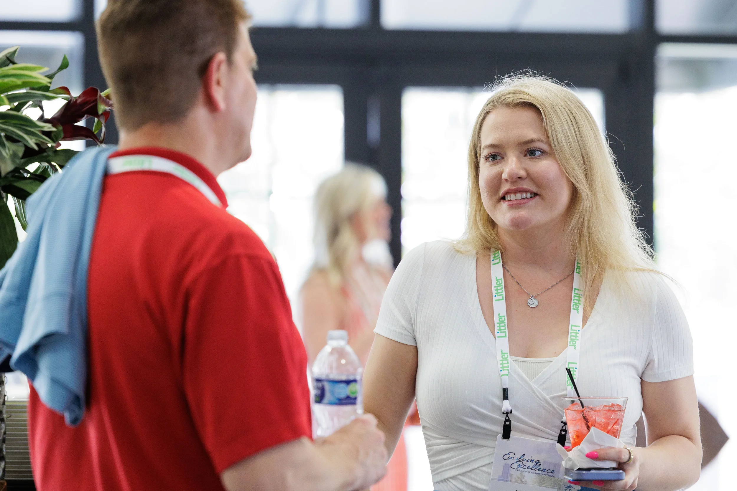 Two attendees with lanyards chat over drinks in bright foyer at Orlando corporate conference