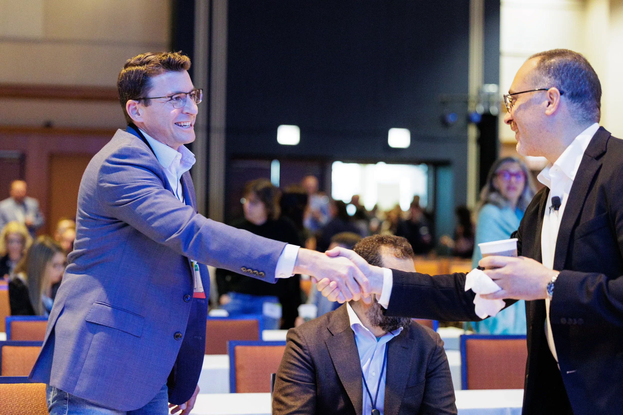 Two attendees shake hands and greet each other in conference room at Orlando industry event