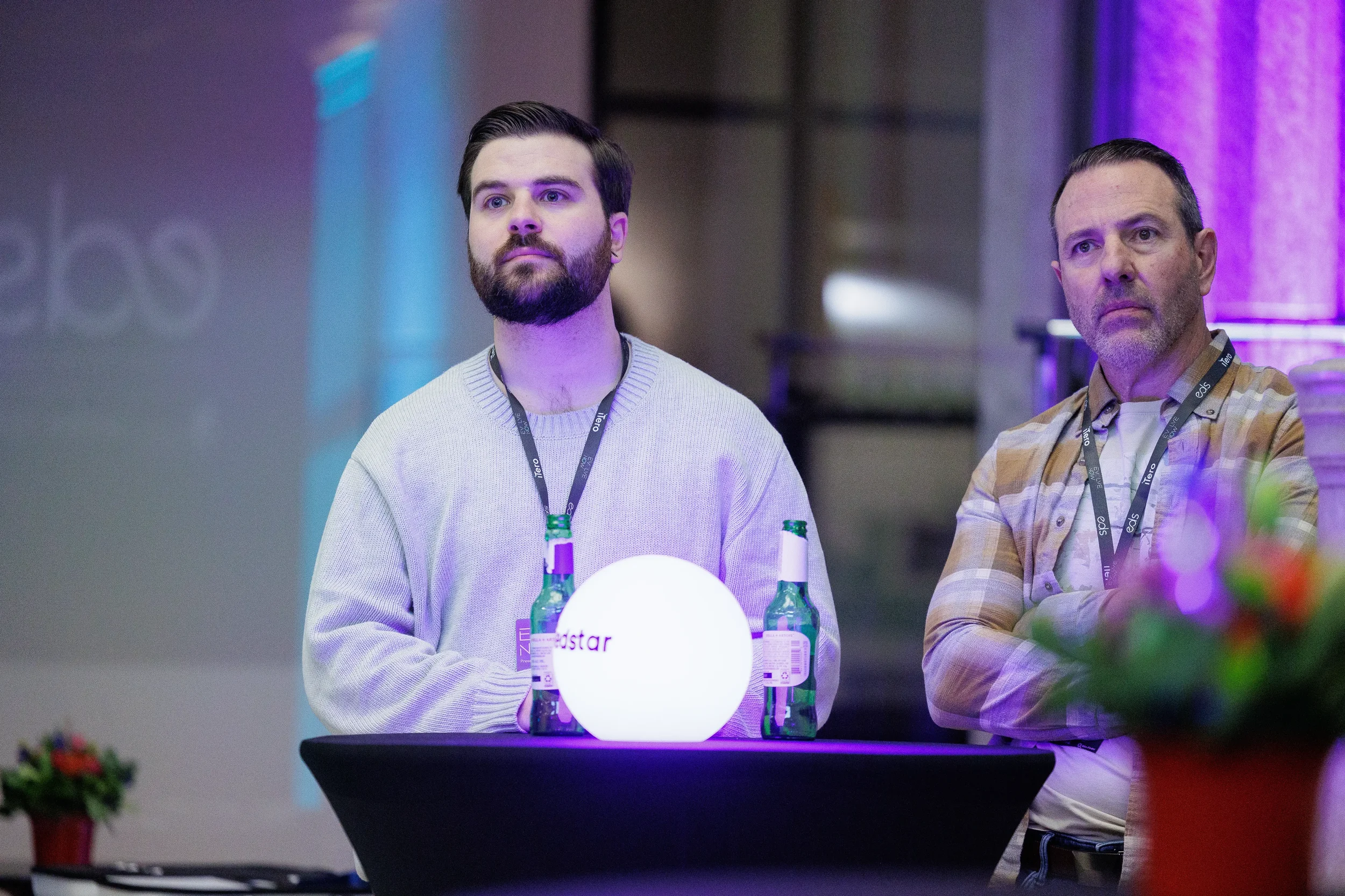 Two attendees with lanyards stand at cocktail table watching session at Chicago corporate event