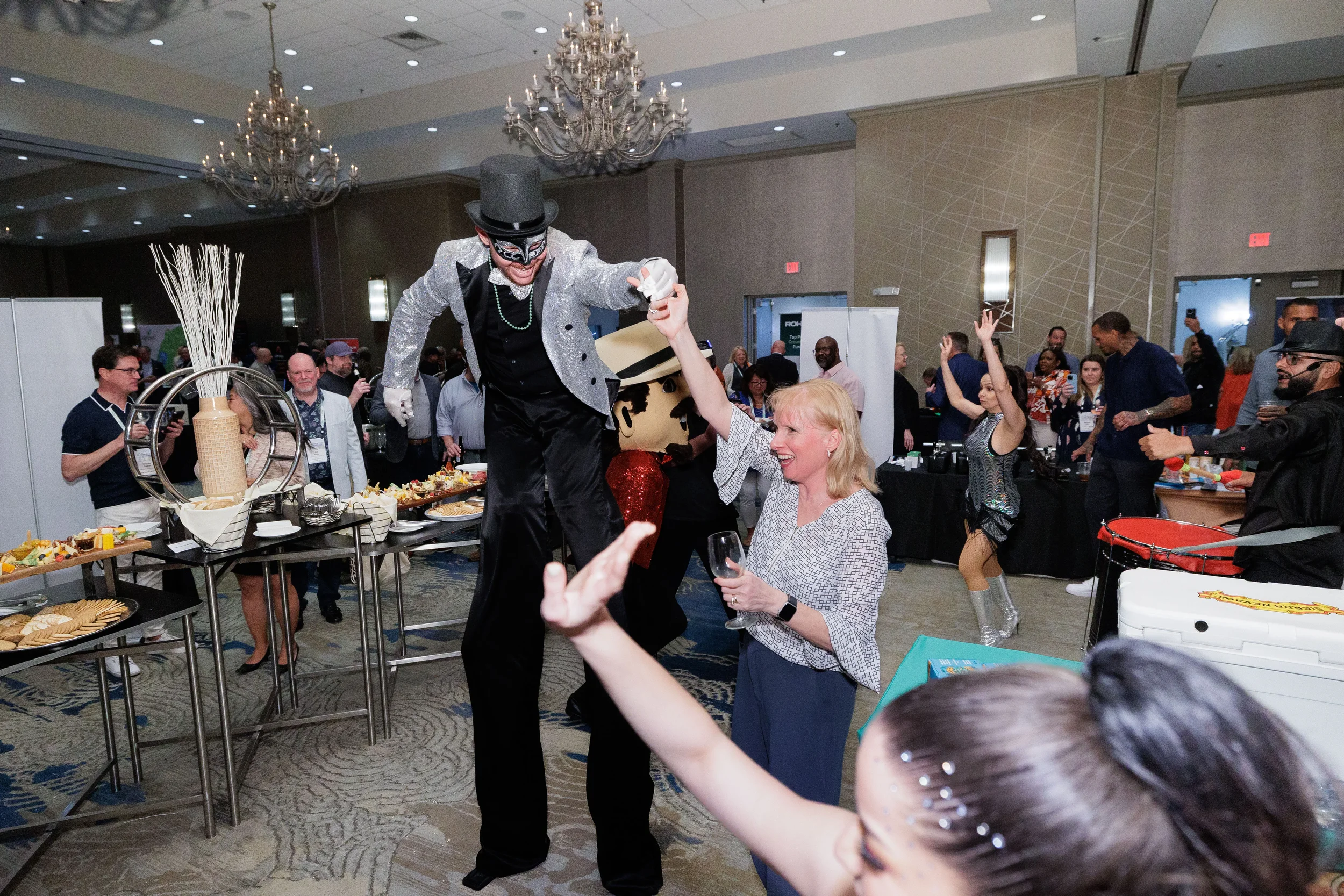 Stilt performer dances with smiling attendee near mascot character at Chicago corporate conference reception